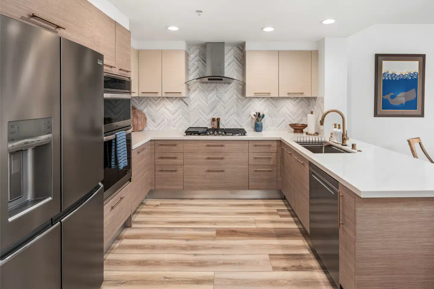 Two-tone condo kitchen with light oak base cabinets, pale wall cabinets, a gas cooktop and a wall-mounted hood