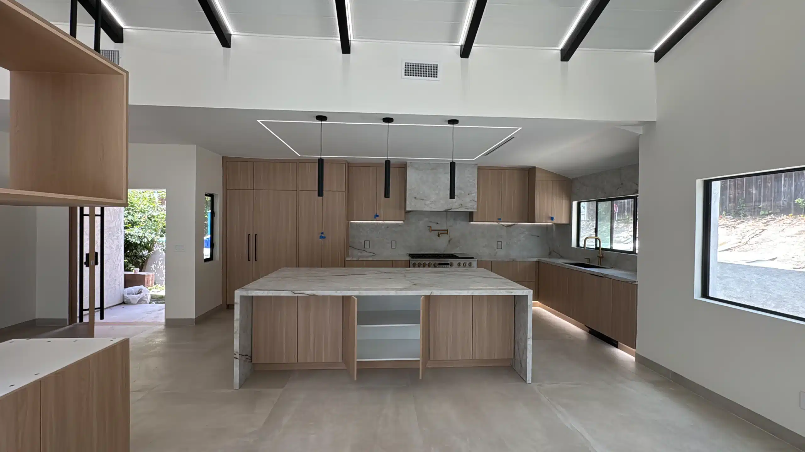 Open-plan kitchen and living area after the Scripps Ranch remodel, with a marble island, light oak cabinetry and black beams across a vaulted ceiling