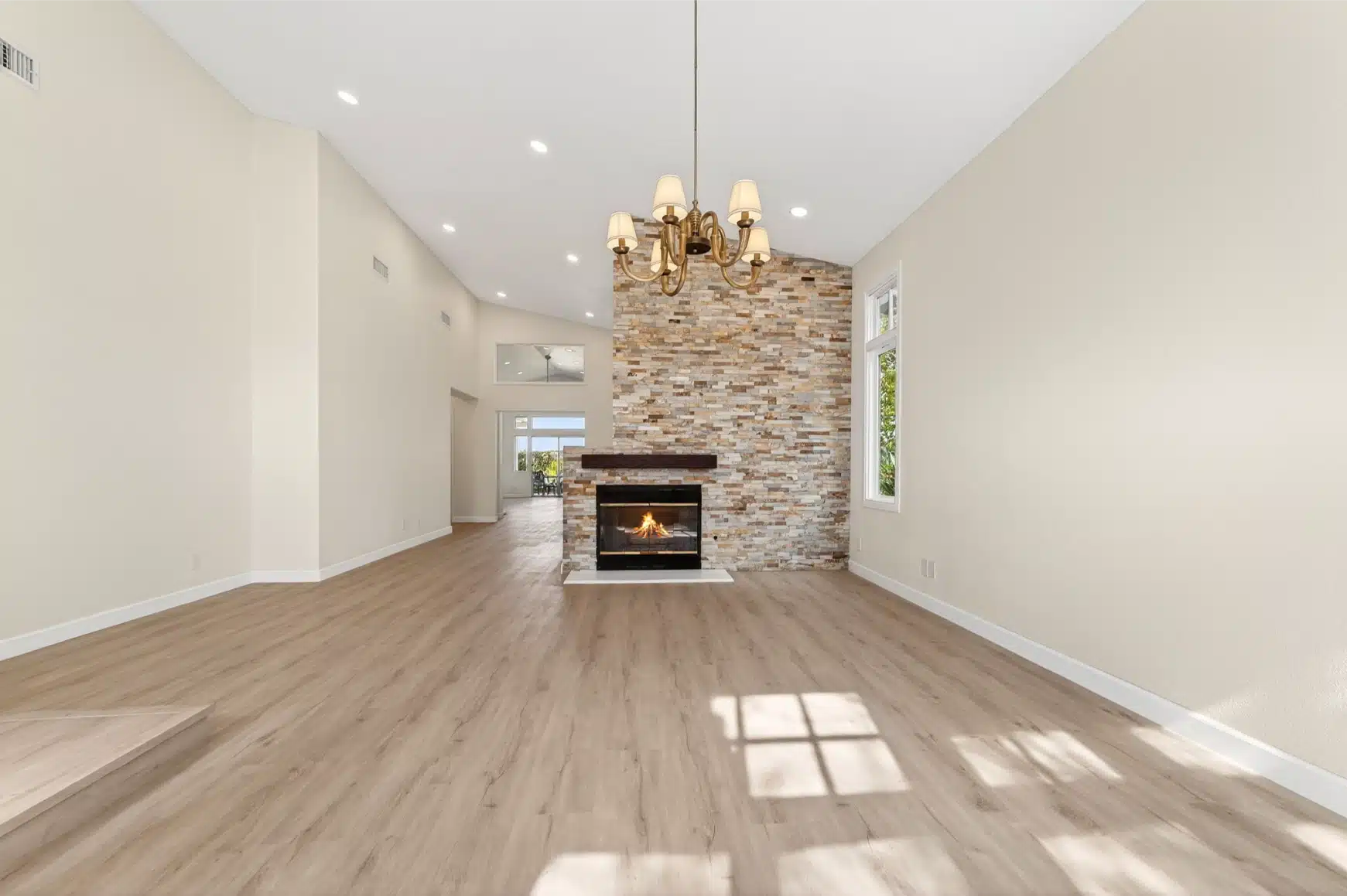 The full length of the remodelled living space, from the chandelier to the stone fireplace