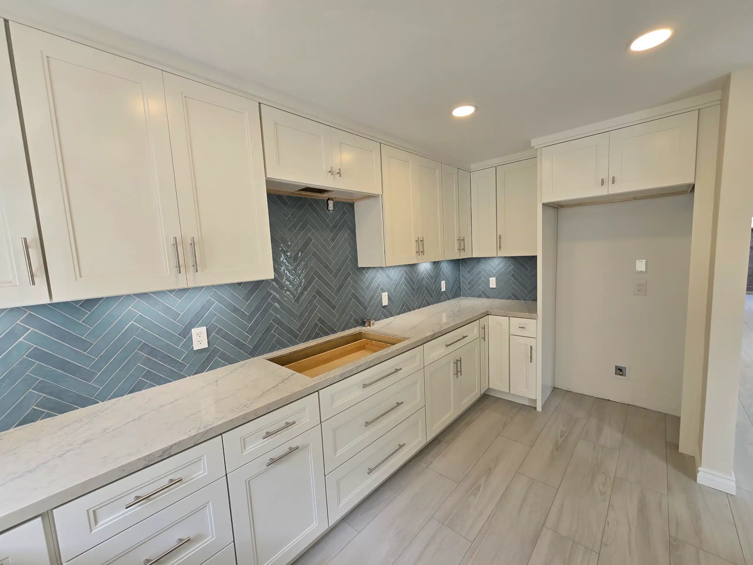 Encinitas kitchen after the remodel, showing the full run of white shaker cabinetry, quartz counters and herringbone tile