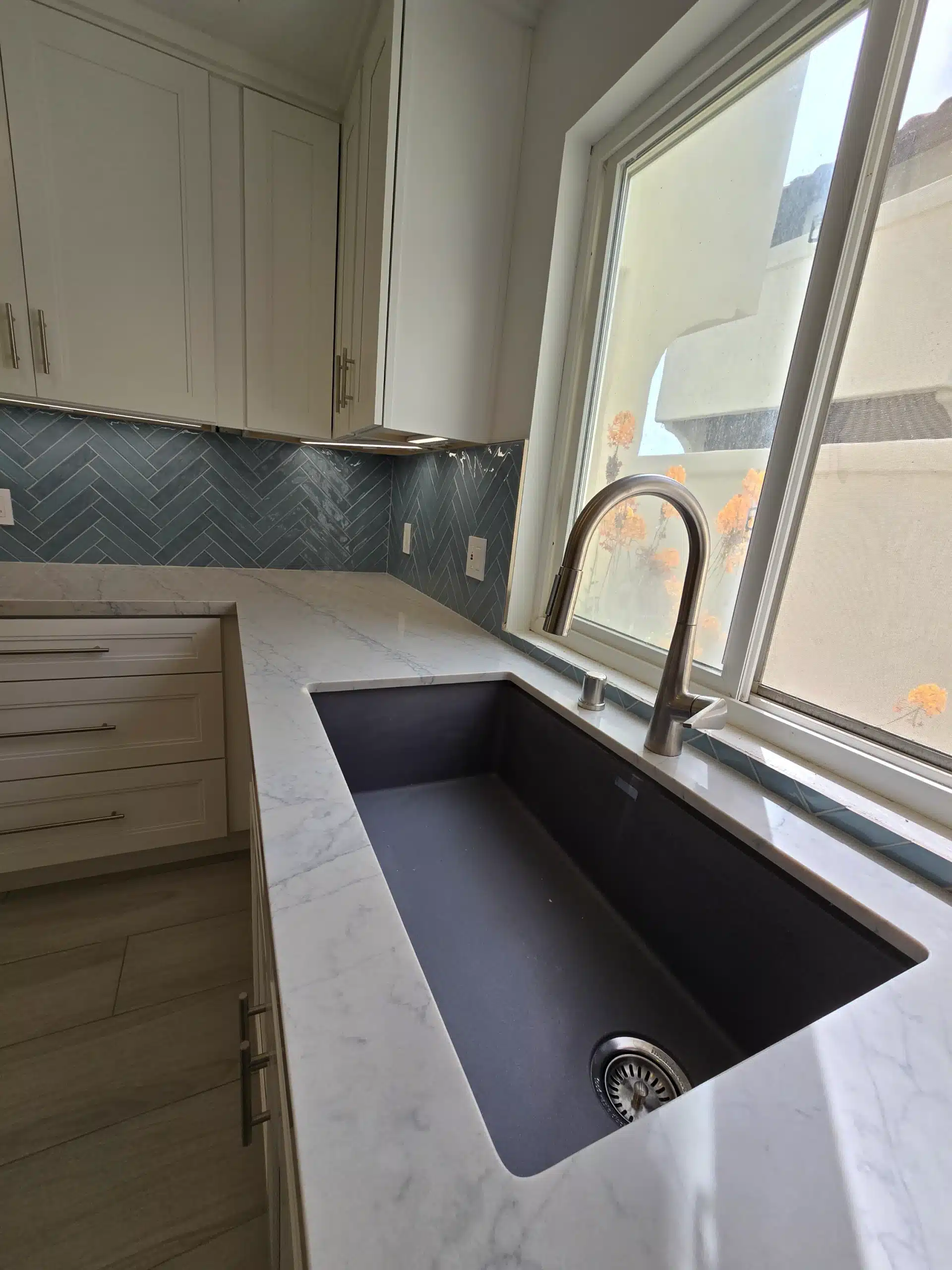 Undermount composite sink and gooseneck tap set into the marble-look quartz counter beneath the kitchen window