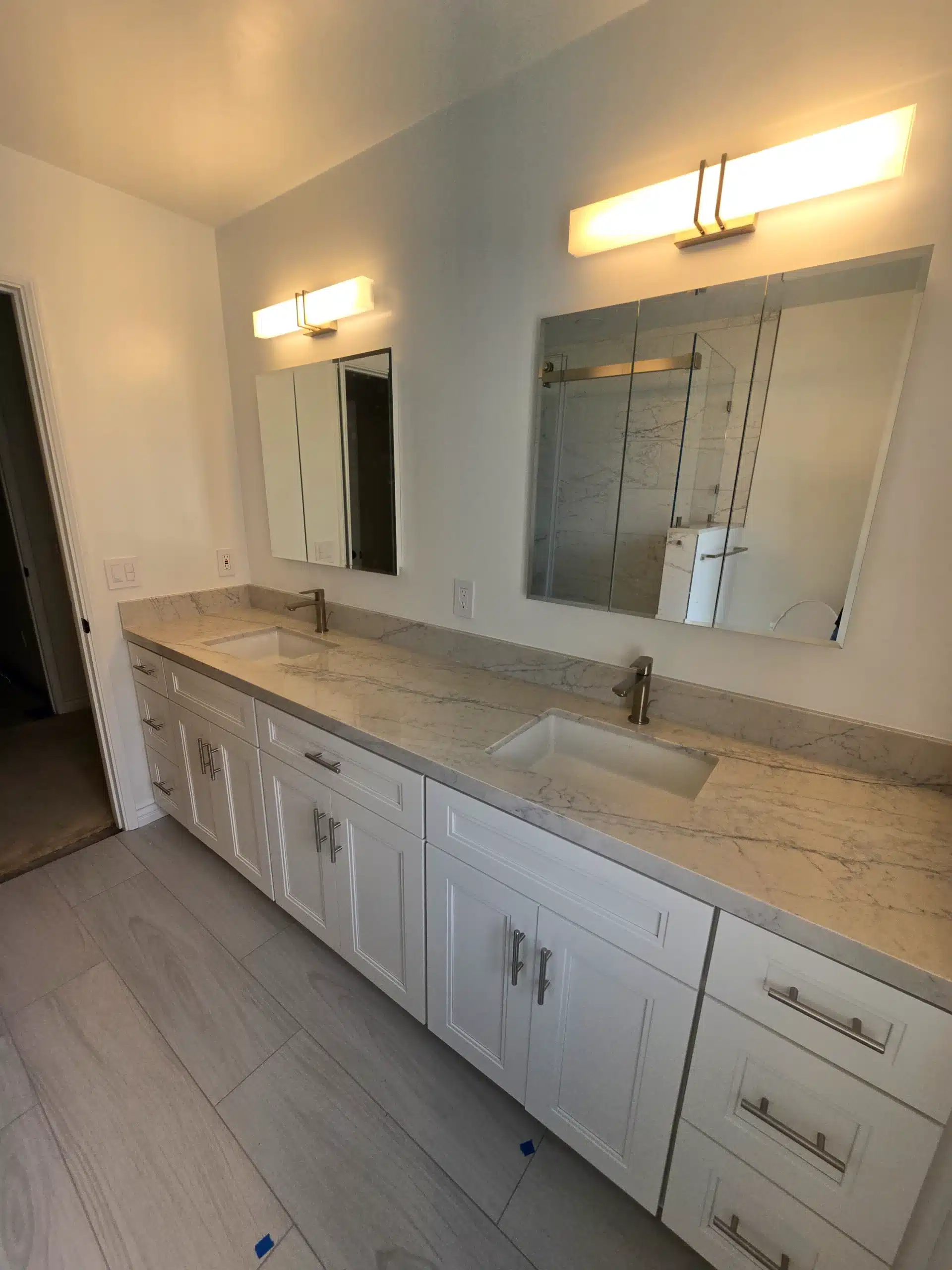 Primary bathroom double vanity with marble-look counter, twin framed mirrors and linear vanity lighting
