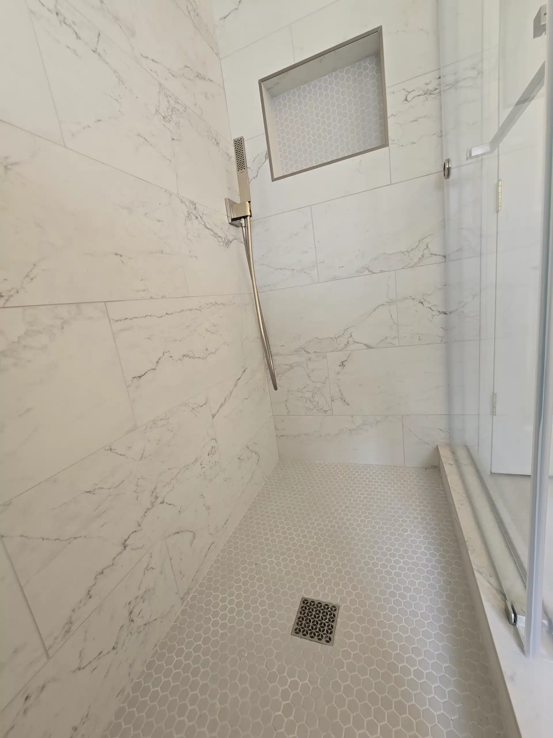 Penny-round mosaic shower floor with a linear drain and marble-look wall tile