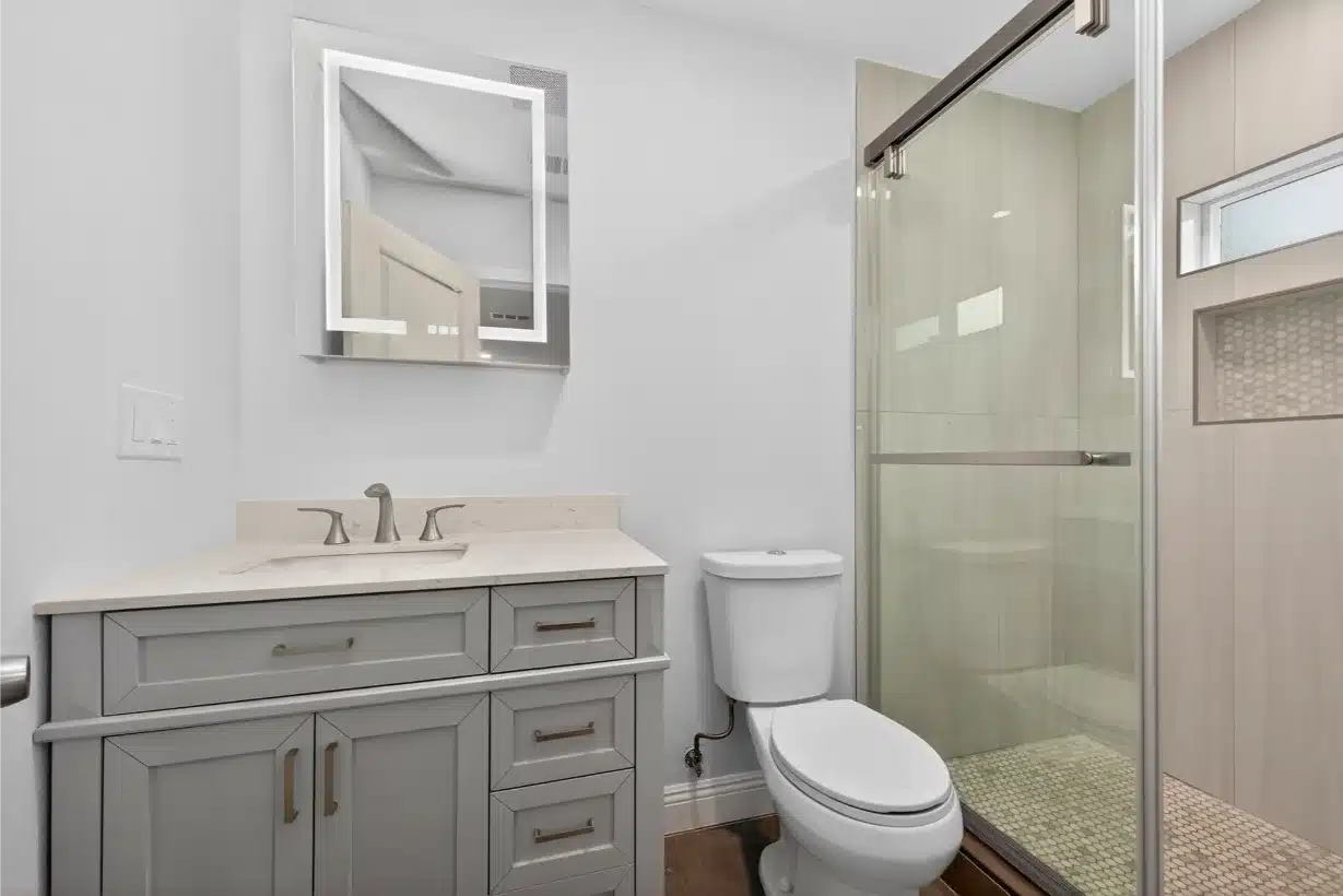 Completed bathroom with a framed vanity, wide mirror and glass shower enclosure