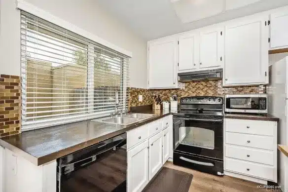 The original kitchen sink wall with white cabinets, a dark speckled counter and a mosaic tile backsplash