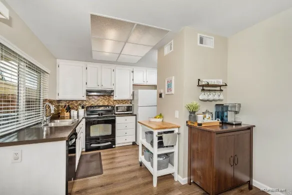The original kitchen with white cabinets, a mosaic tile backsplash and black appliances, open to the dining area
