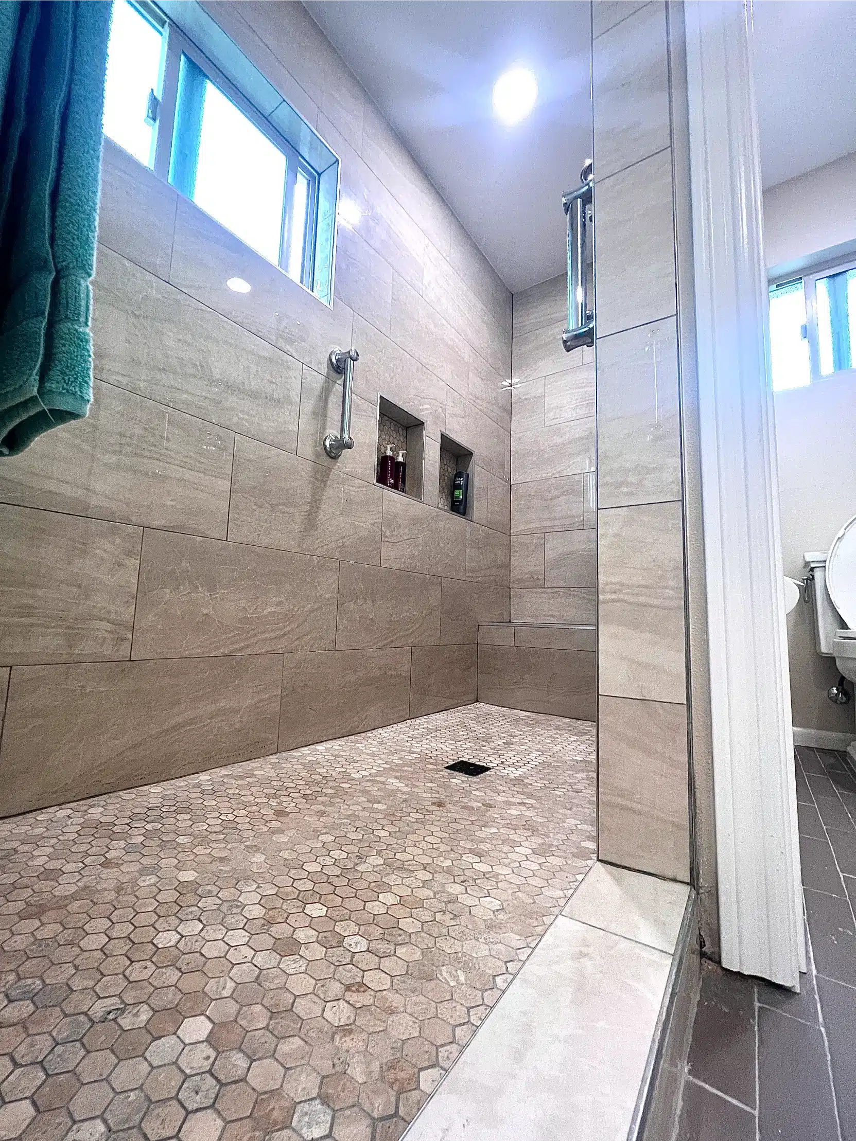 The finished accessible shower with grab bars, a bench and a pebble floor