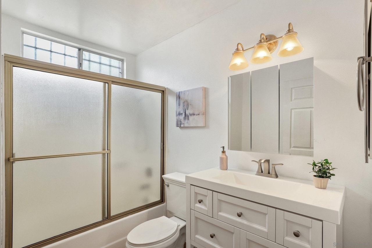 The La Mesa bathroom before the remodel, with framed sliding shower doors over the tub and a dated vanity