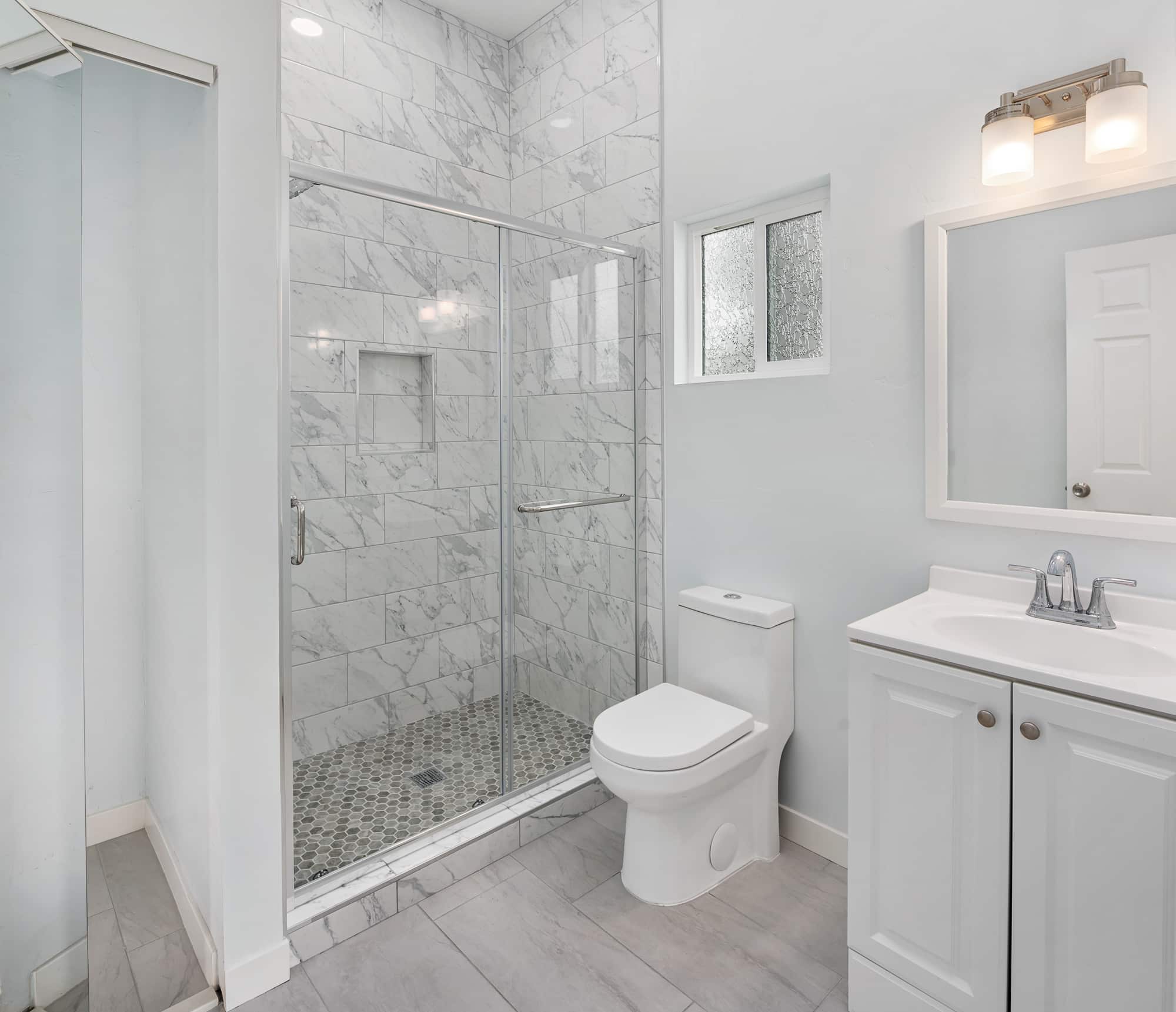 Walk-in shower finished in marble-look wall tile with a glass panel, in a completed San Diego bathroom