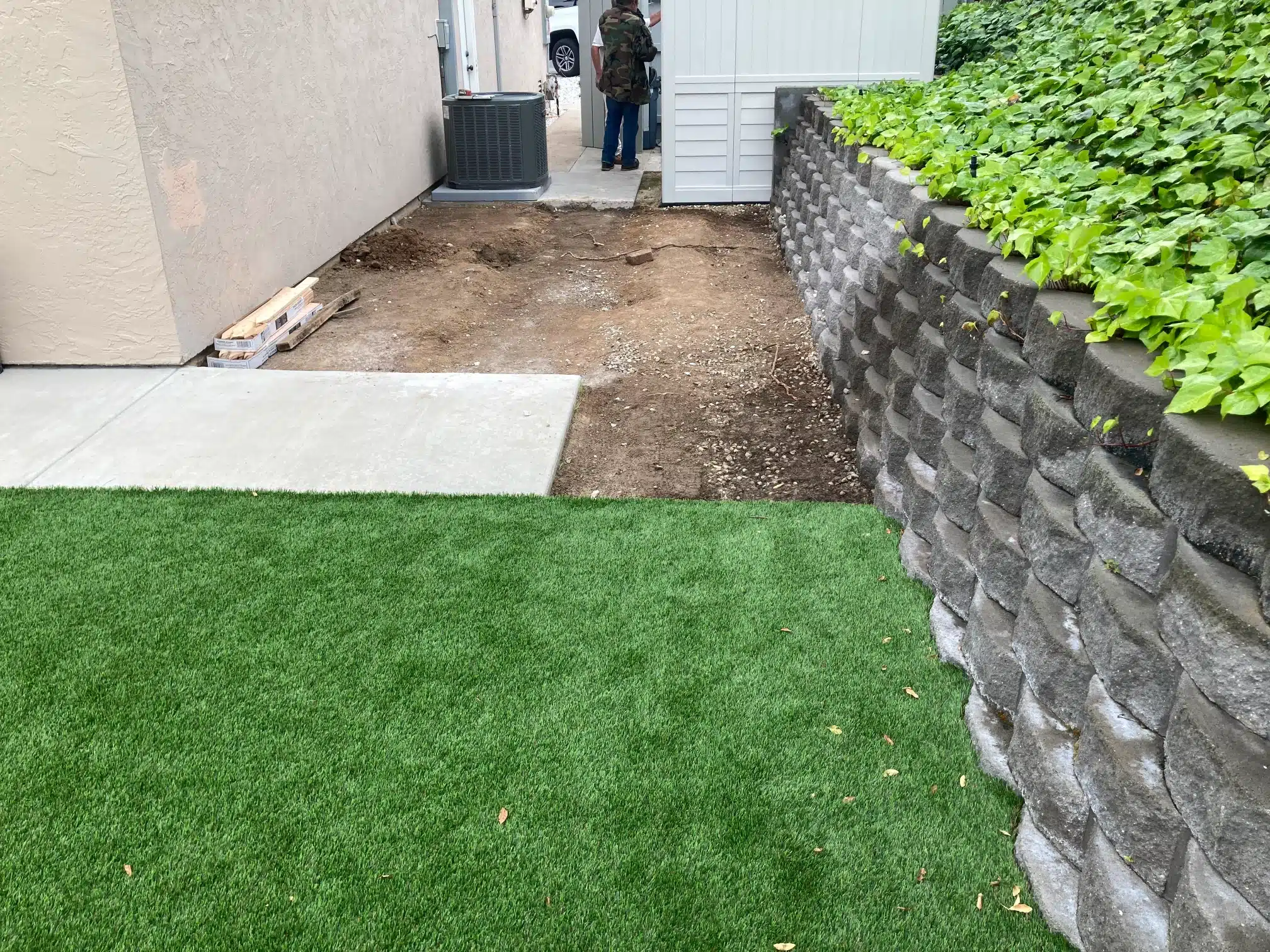 The side yard before work, with turf and a retaining wall holding the grade
