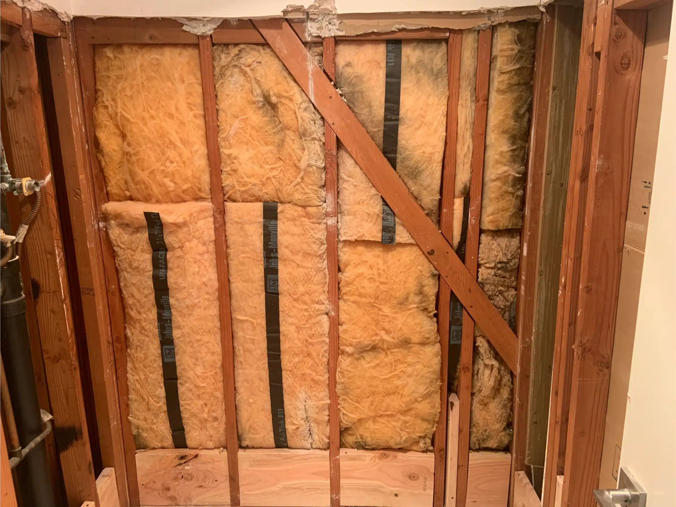 The shower wall stripped to the studs with insulation and bracing visible