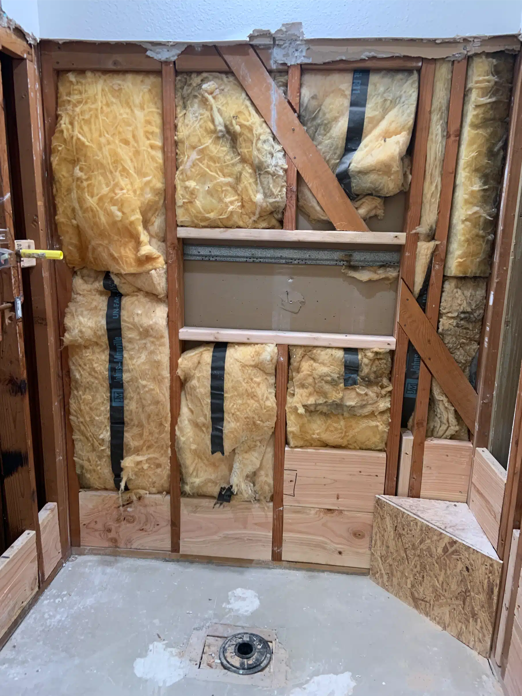Bathroom taken back to the studs, showing insulation, the roughed-in shower valve and blocking framed around the niche opening