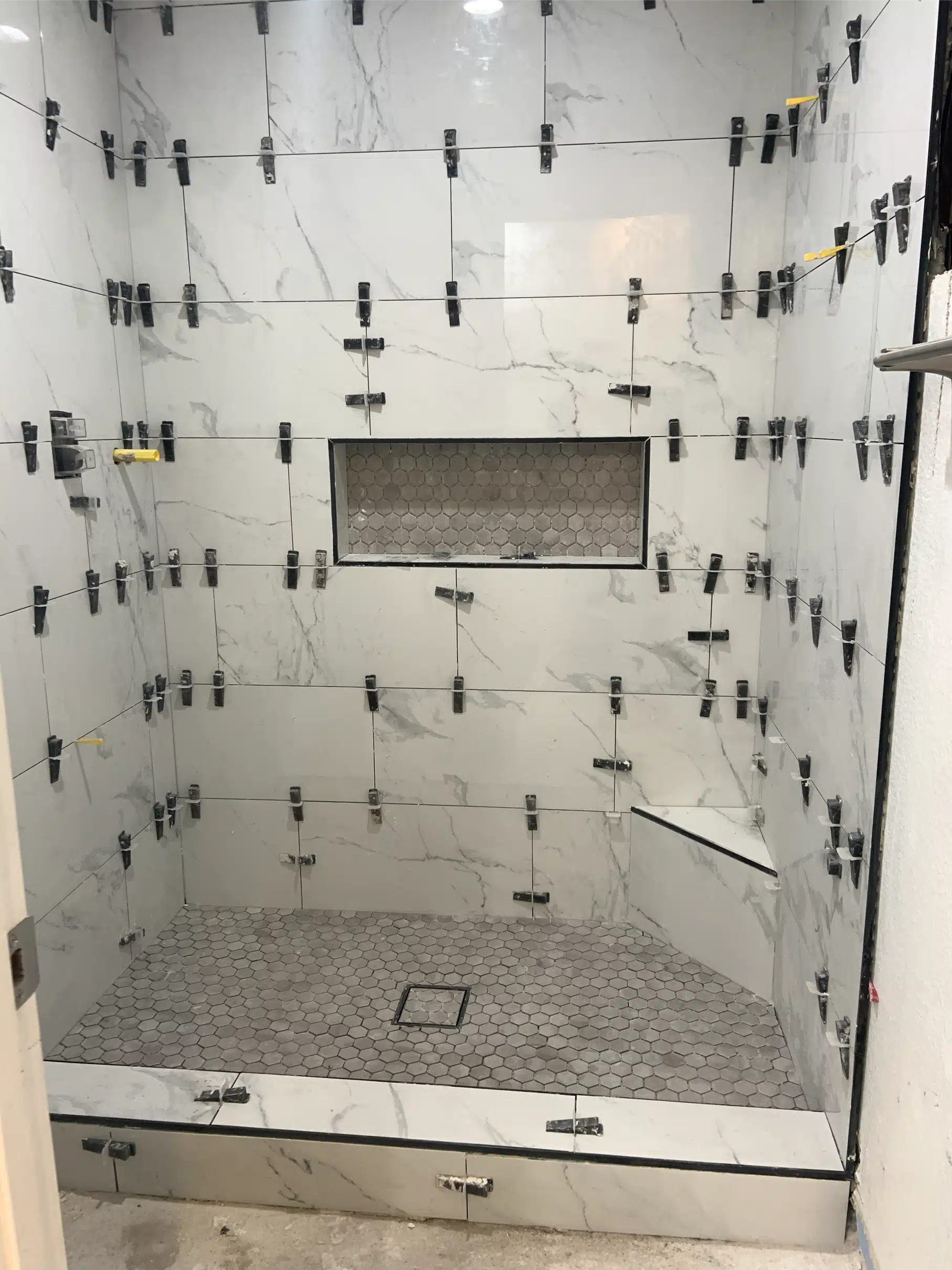 Shower wall tile set with levelling clips still in place, the mosaic niche band and the mosaic shower floor laid