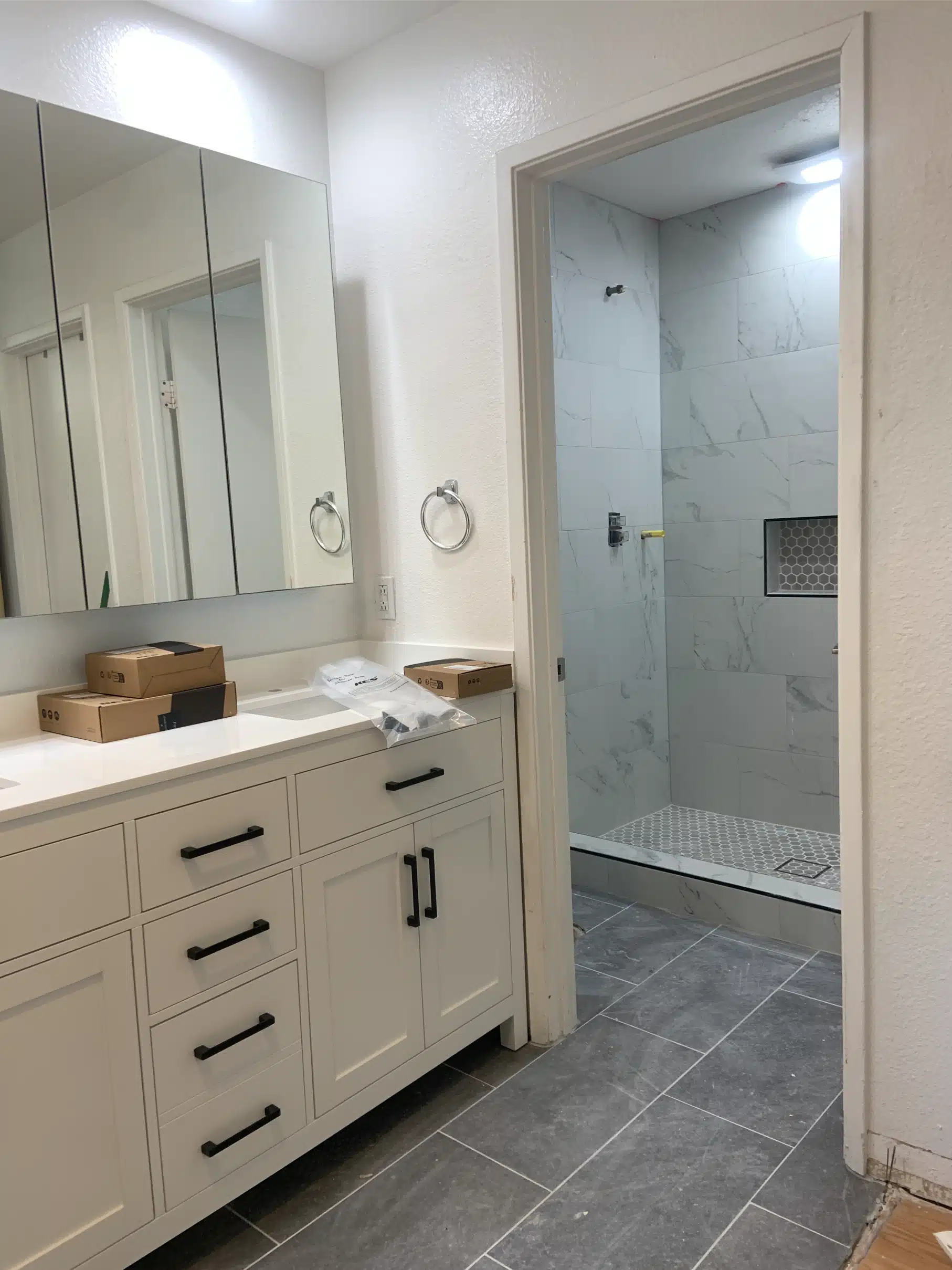 Completed San Diego bathroom with a white shaker vanity, black hardware and the glass walk-in shower beyond