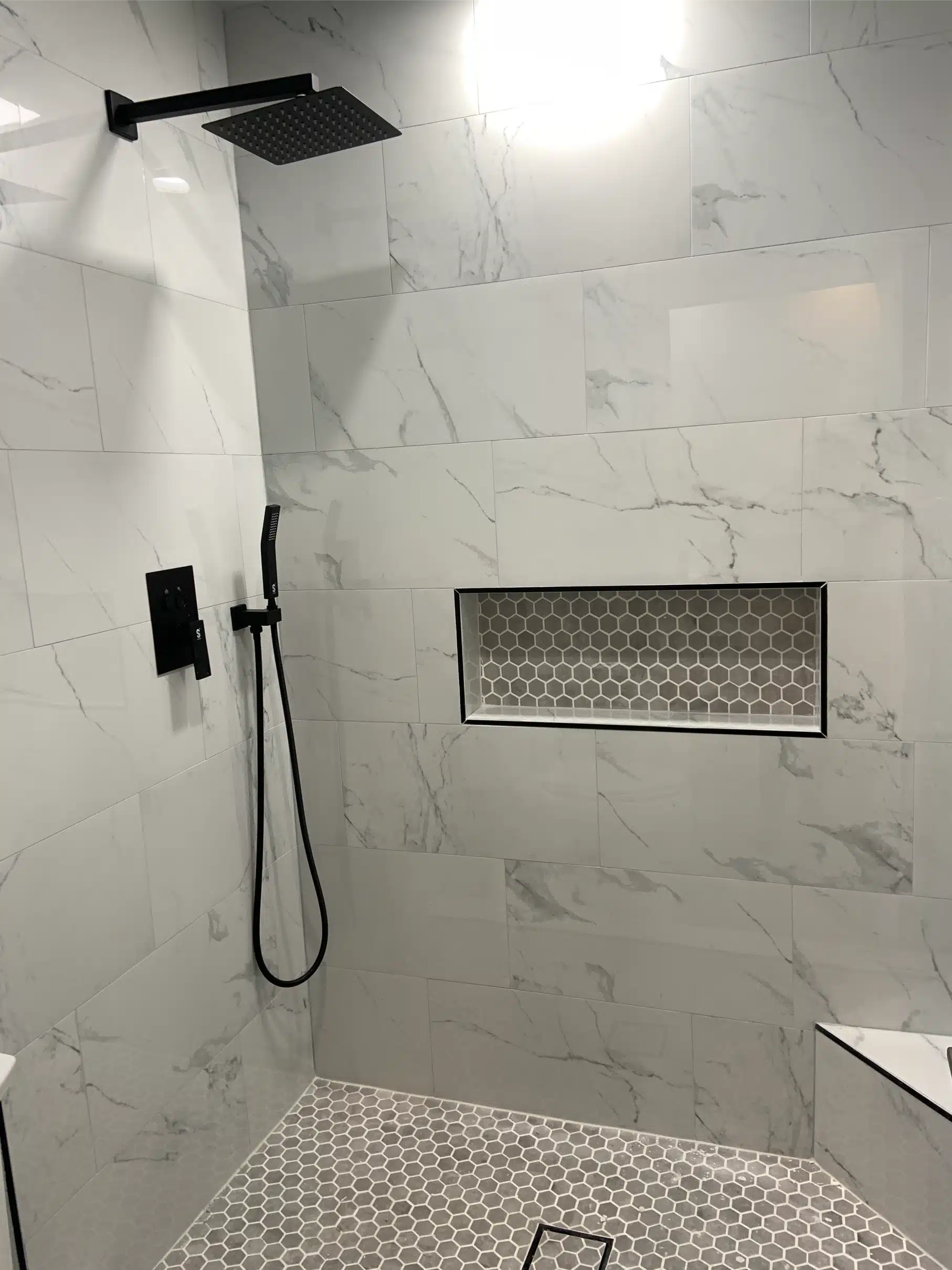 Finished walk-in shower with a matte black shower set, handheld on a slide bar and a recessed mosaic niche