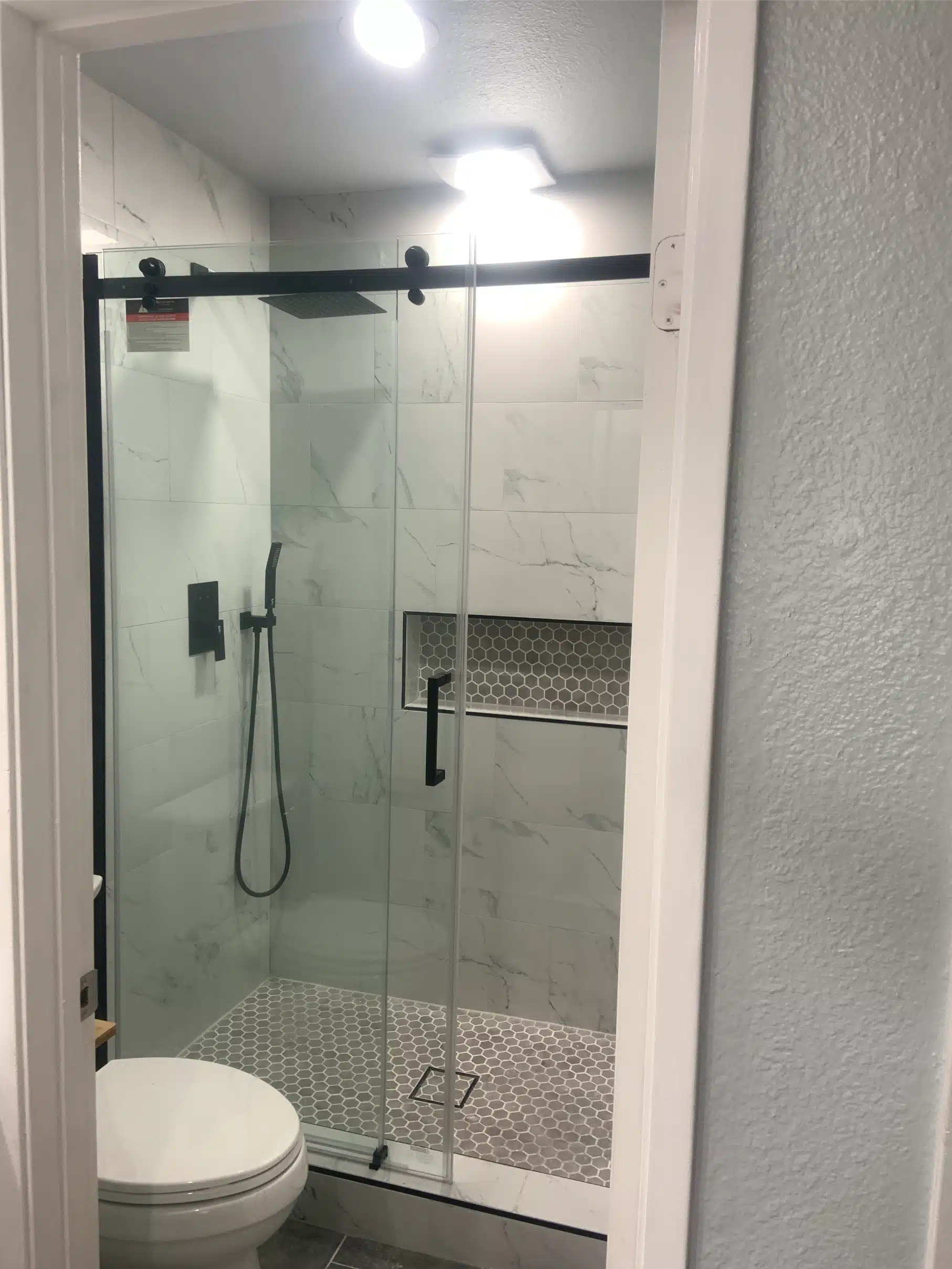 Finished bathroom with a black-framed sliding glass shower enclosure and plank-format floor tile