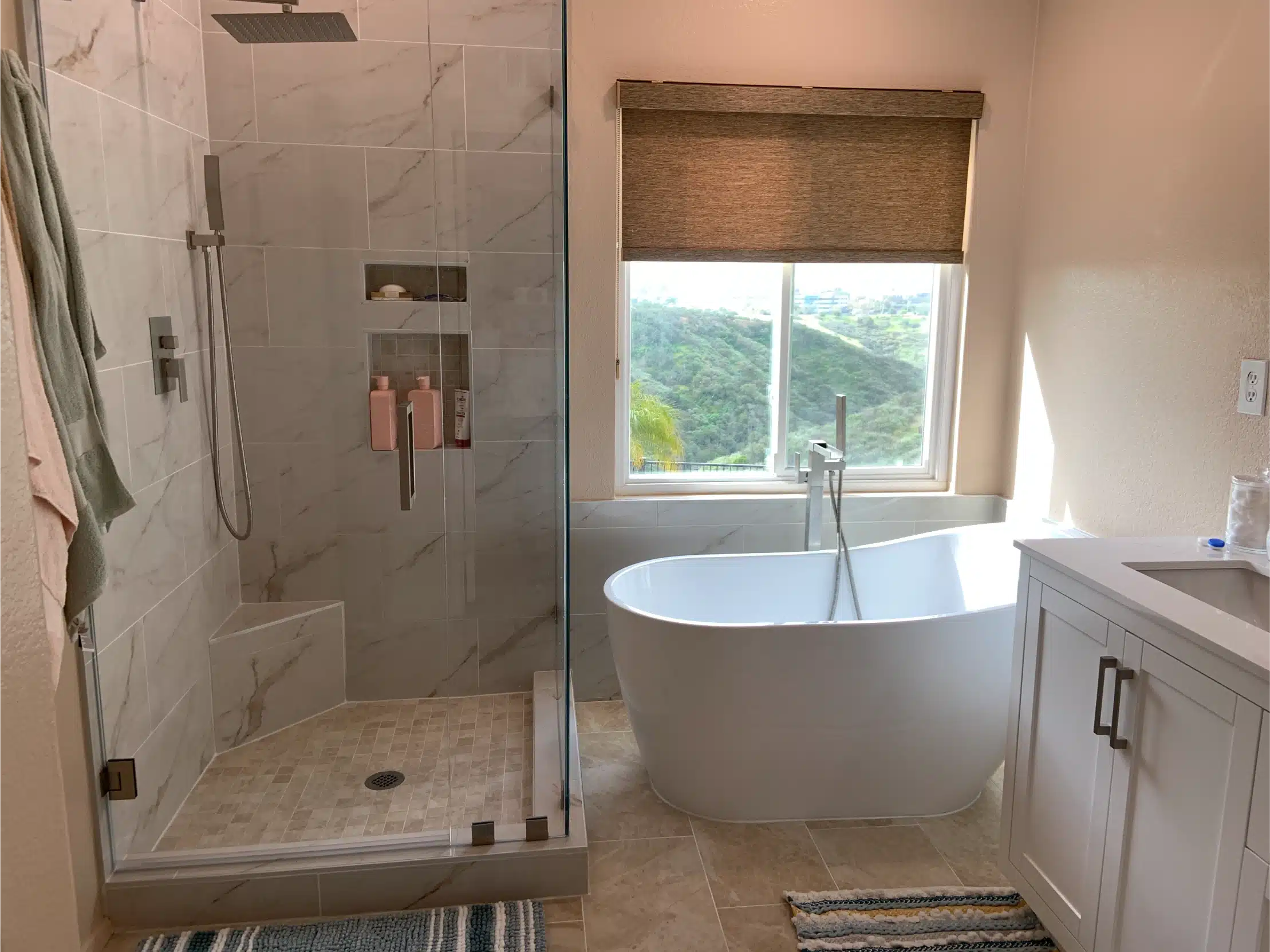 The finished bathroom with the freestanding tub under the window and the curbless shower beside it