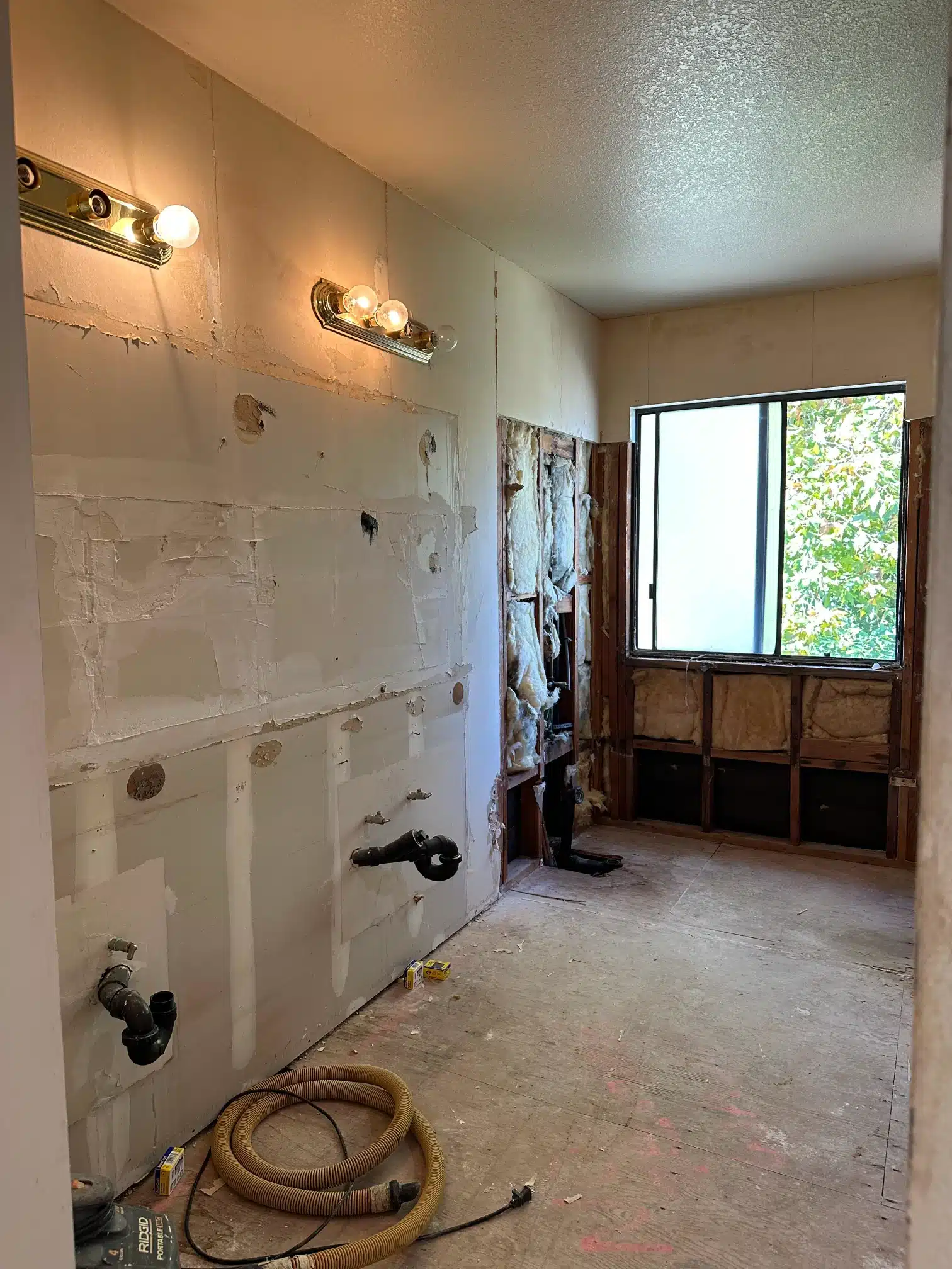 The bathroom stripped out with plumbing exposed and the vanity removed