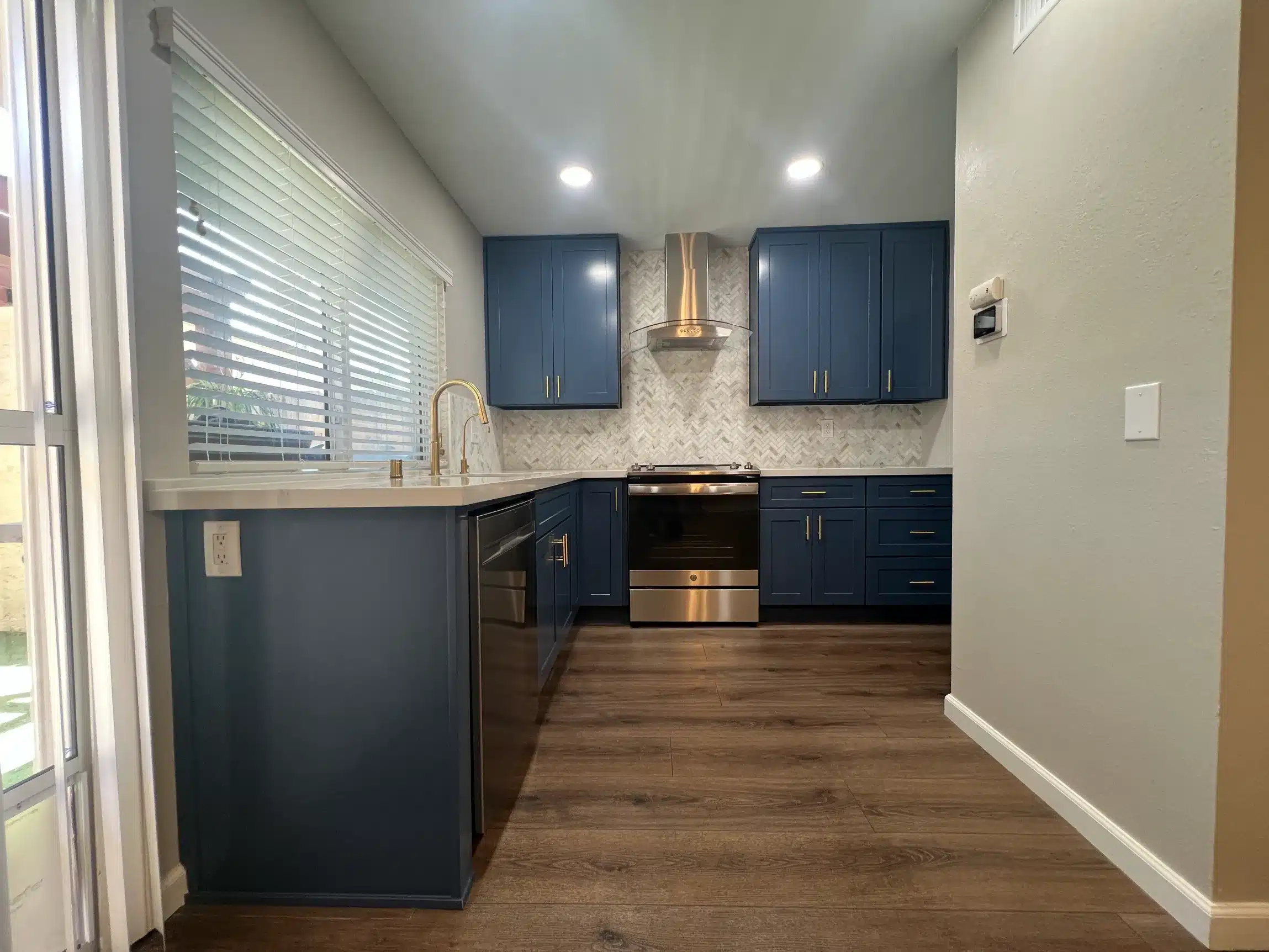 The finished kitchen seen from the doorway with navy cabinetry on both runs beneath recessed lighting