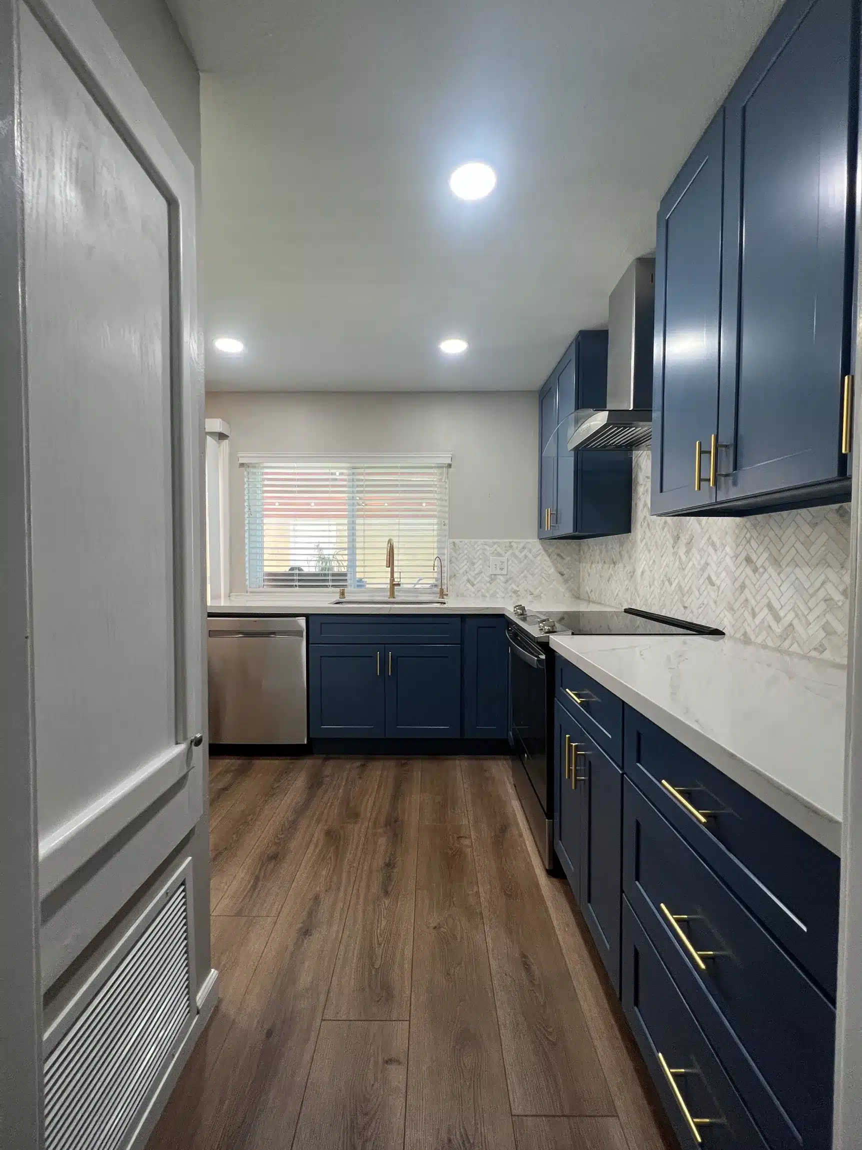 The kitchen seen along the hallway approach across new wood-look flooring