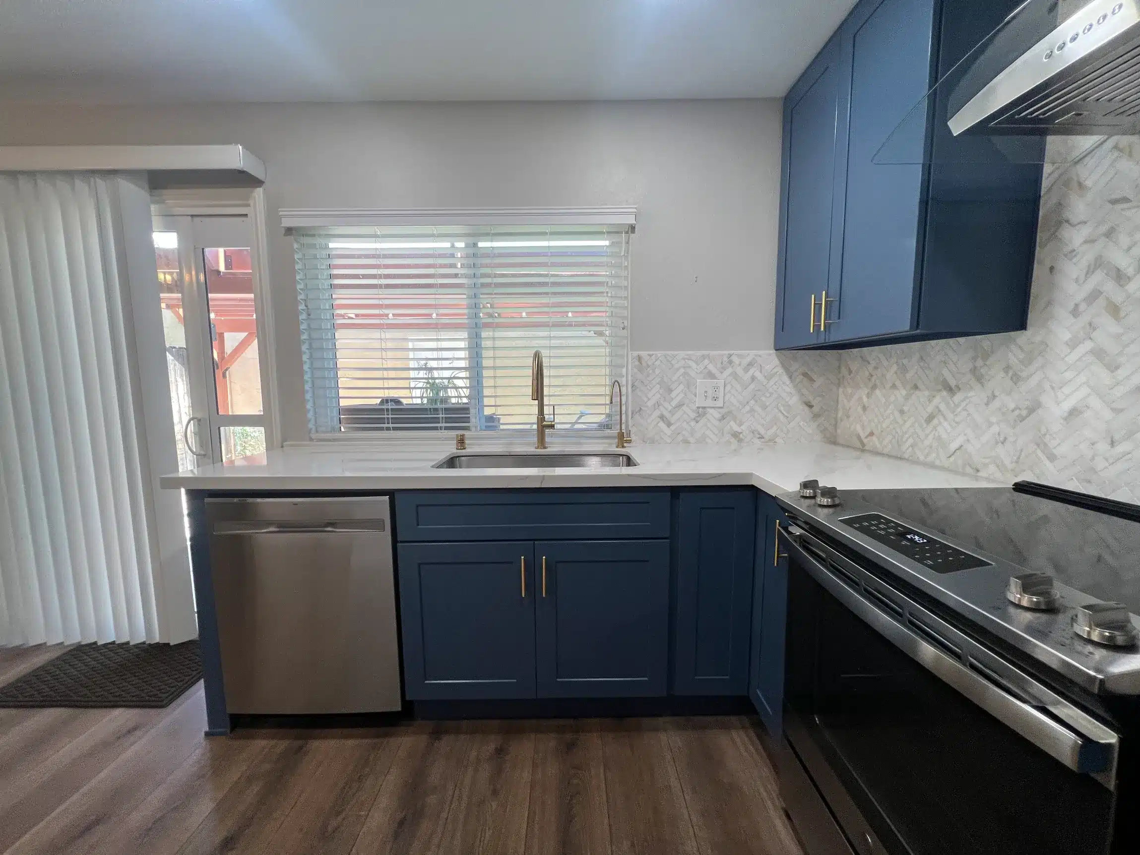 Stainless sink with a brushed gold faucet set beneath the window against the veined backsplash