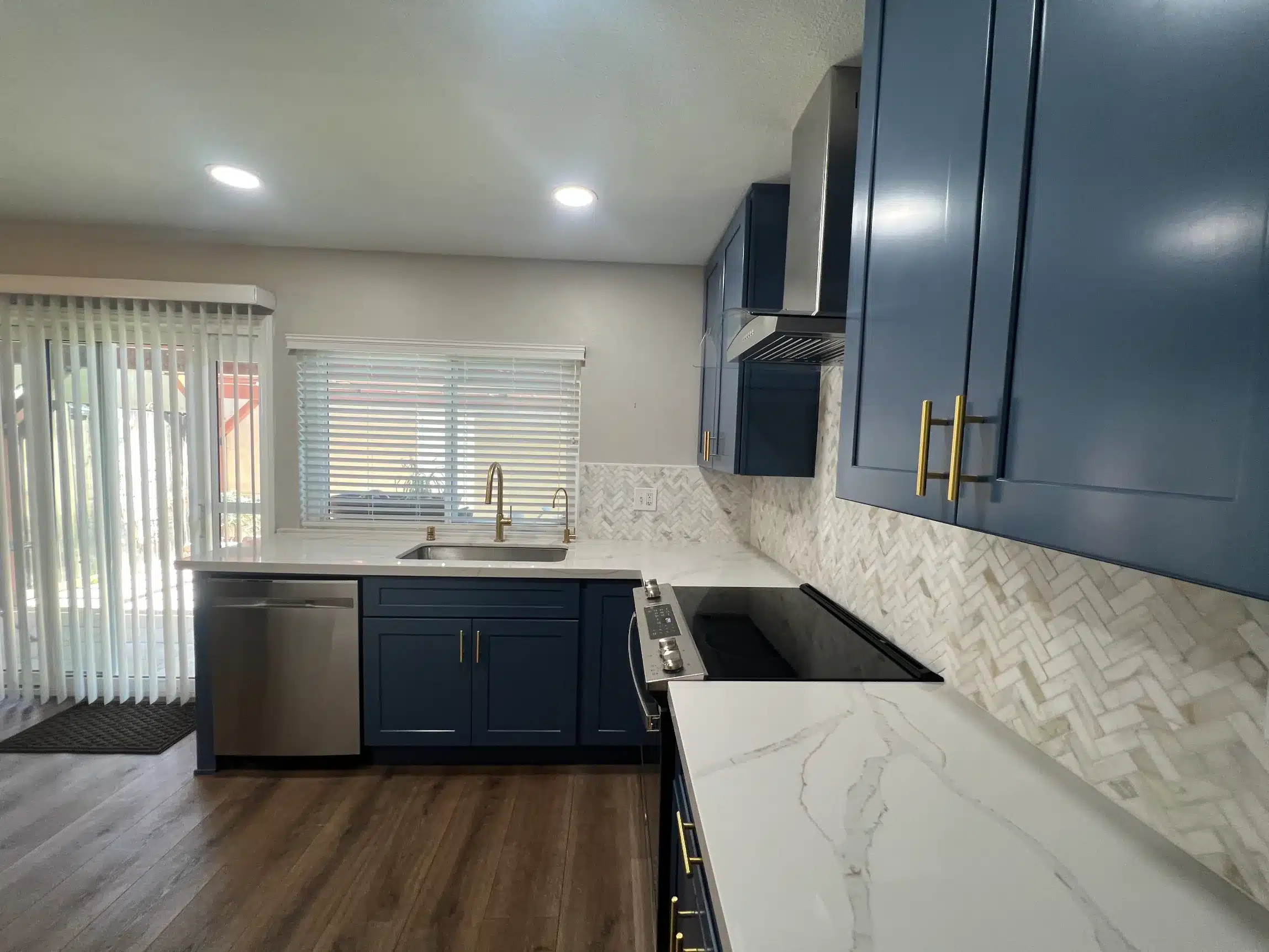 The counter run with the cooktop and sheer curtains drawn at the window beyond