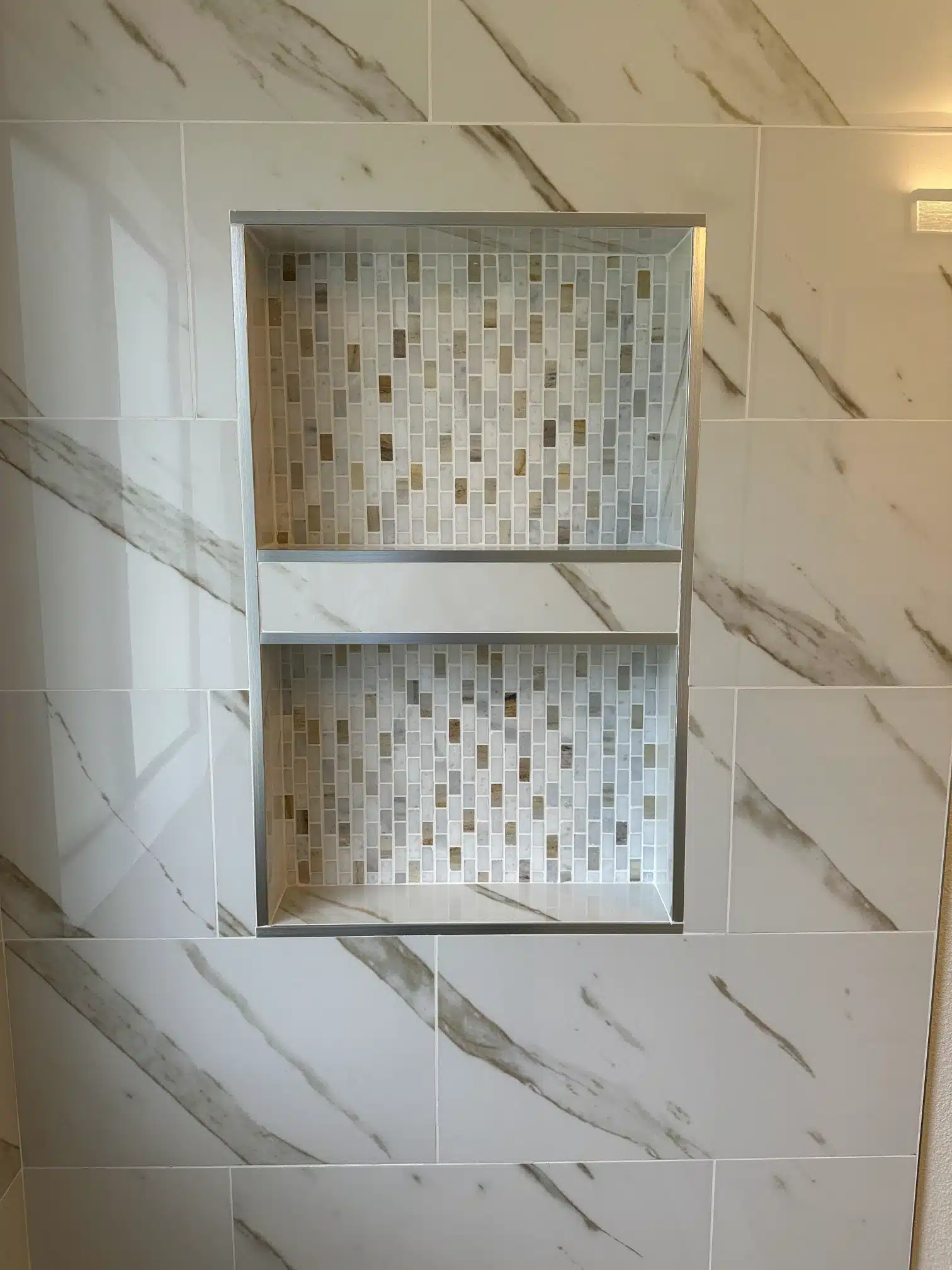 Twin shower niches formed into the tile field with a mosaic back
