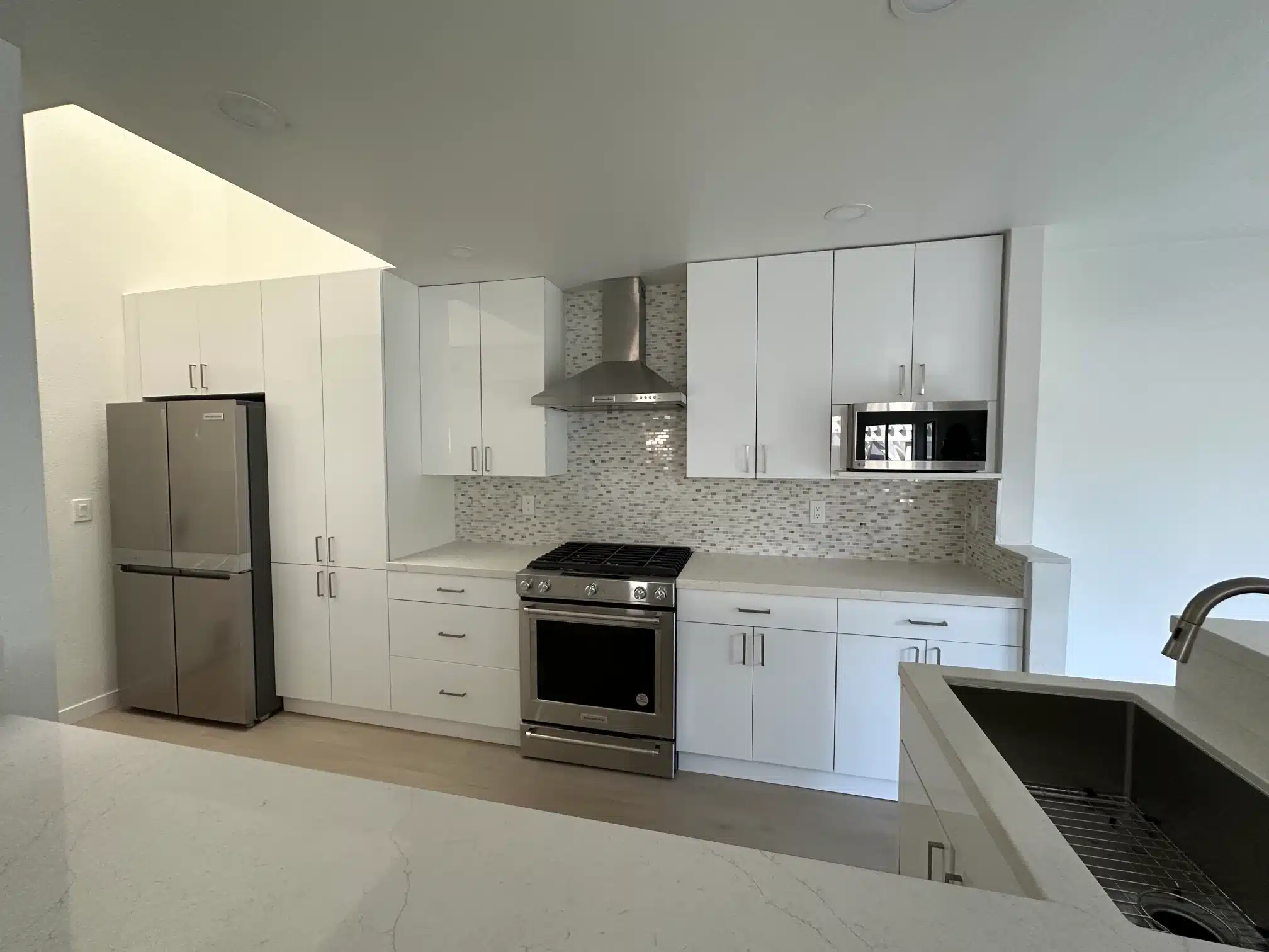 The finished kitchen with white cabinetry, a wall-mounted hood and stainless appliances