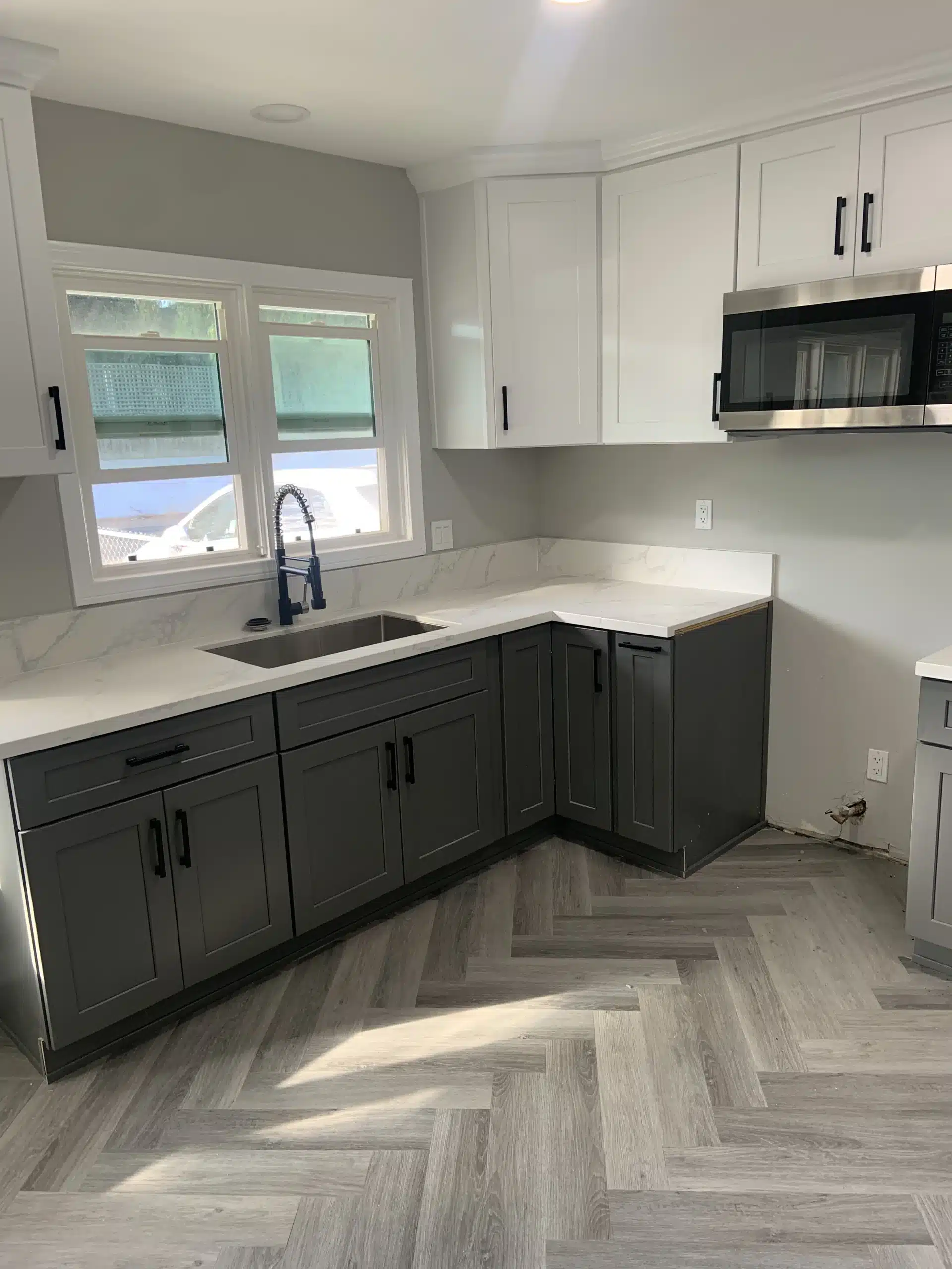 Completed Del Mar kitchen with dark base cabinets, white wall cabinets, a black sink and a window above