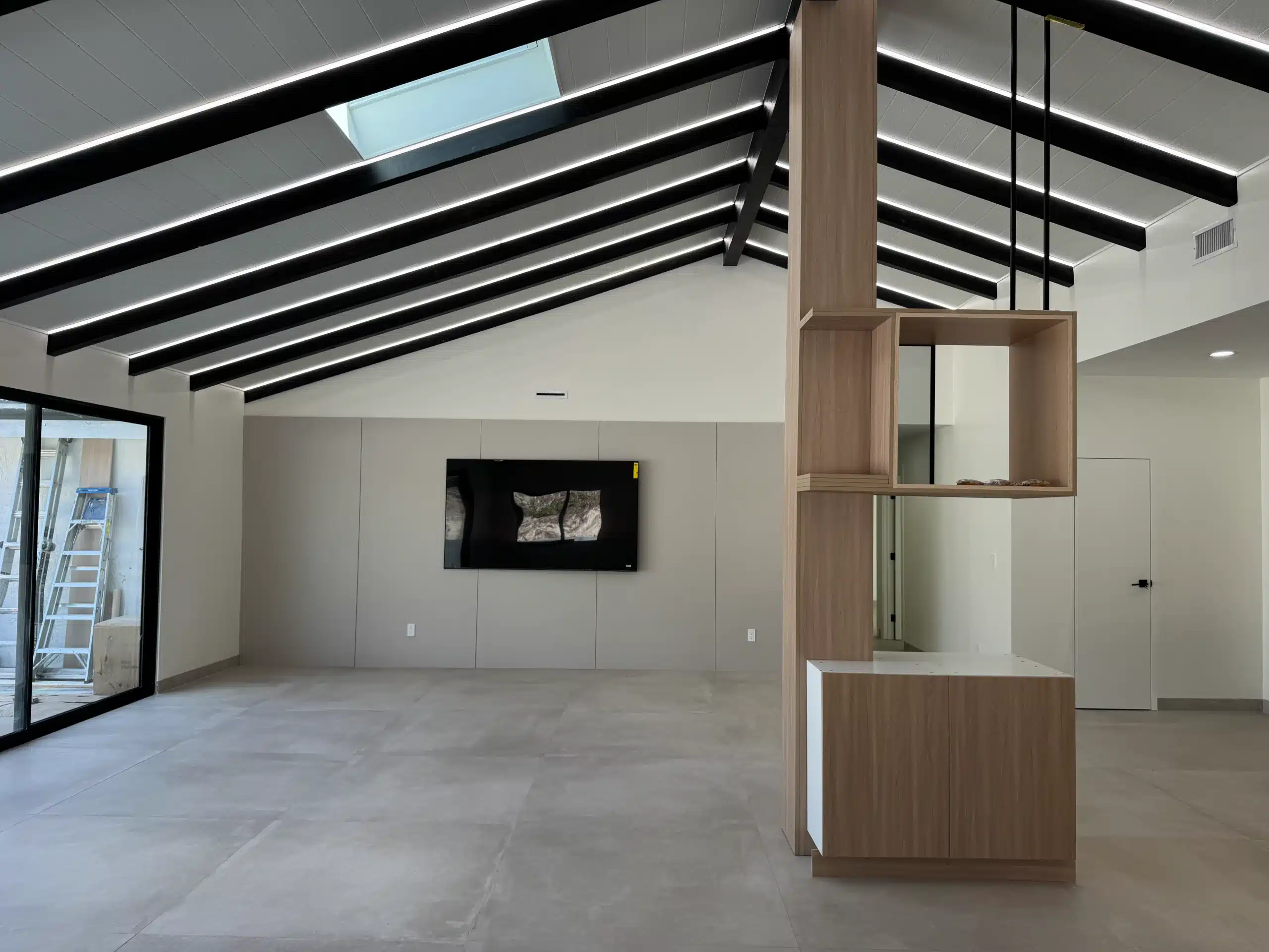 Living area with a linear fireplace set into a dark stone surround, beneath a vaulted ceiling with exposed black beams