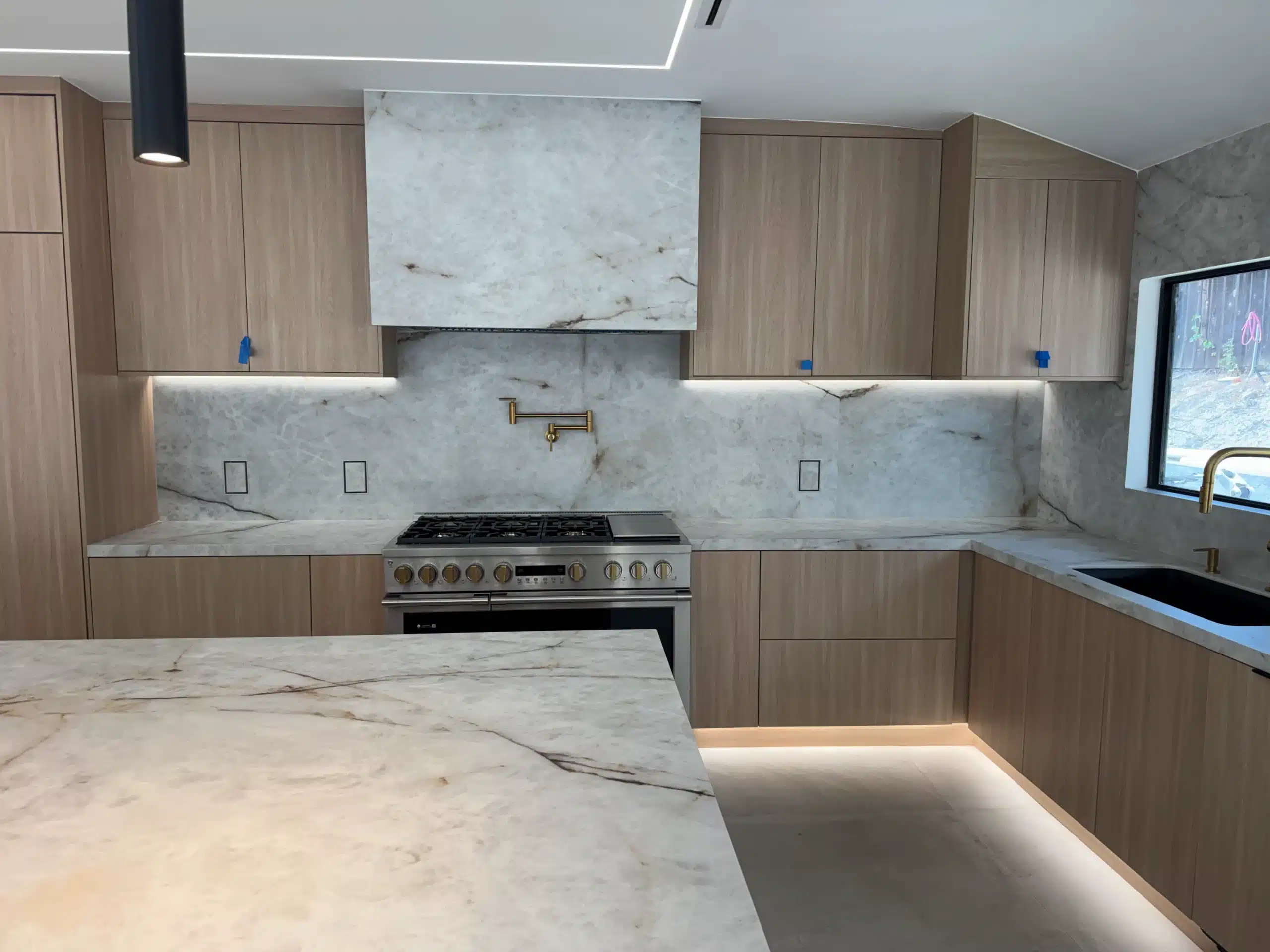 Range wall with a full-height marble slab backsplash and integrated lighting beneath the oak cabinetry