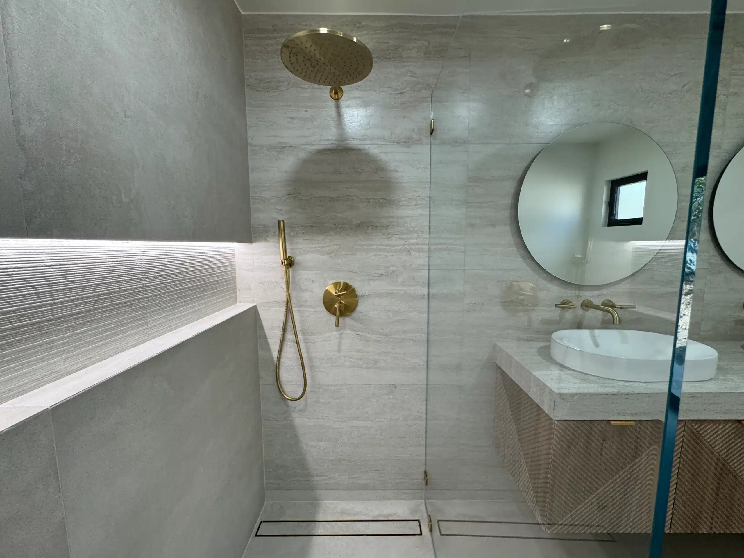 Curbless walk-in shower with frameless glass, brass shower set and a stone-look porcelain bench