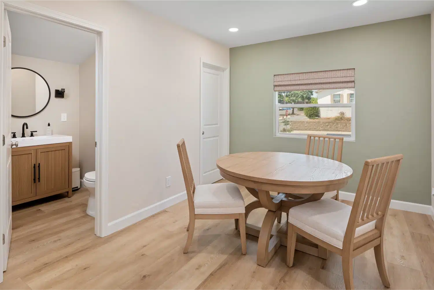 Dining room with a round oak table and chairs against a sage green accent wall