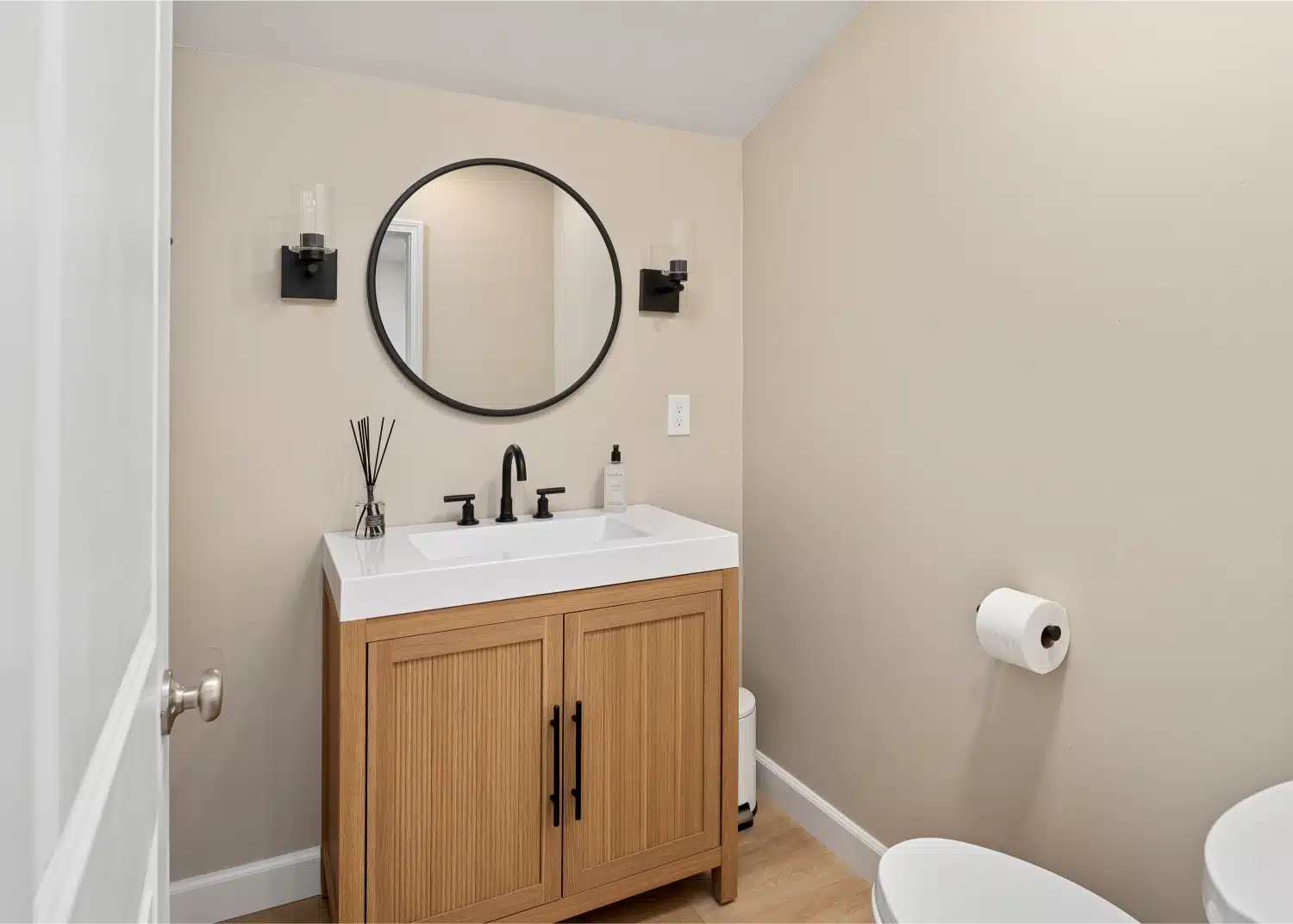 Powder bathroom with an oak vanity, round black-framed mirror and matte black fixtures