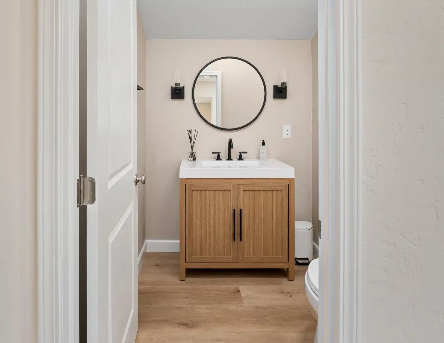 Bathroom vanity in warm oak with a white counter, seen through the doorway