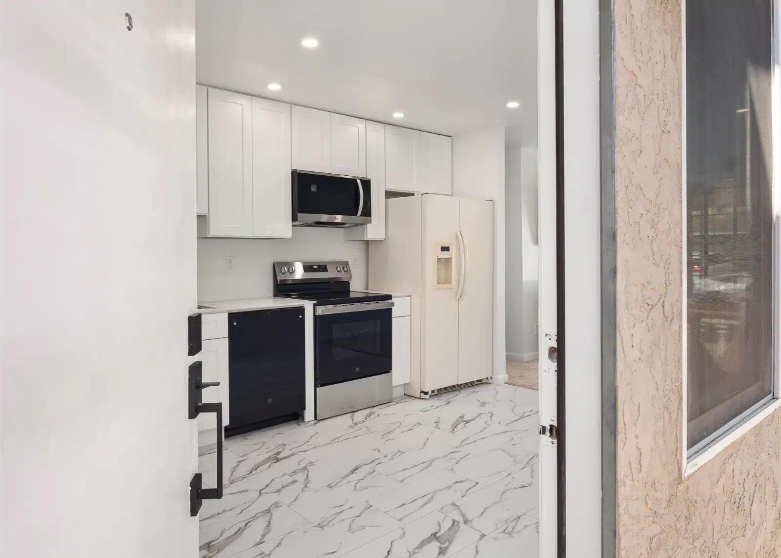 Kitchen in the addition, seen from the entry, with white cabinets and marble-look tile floor