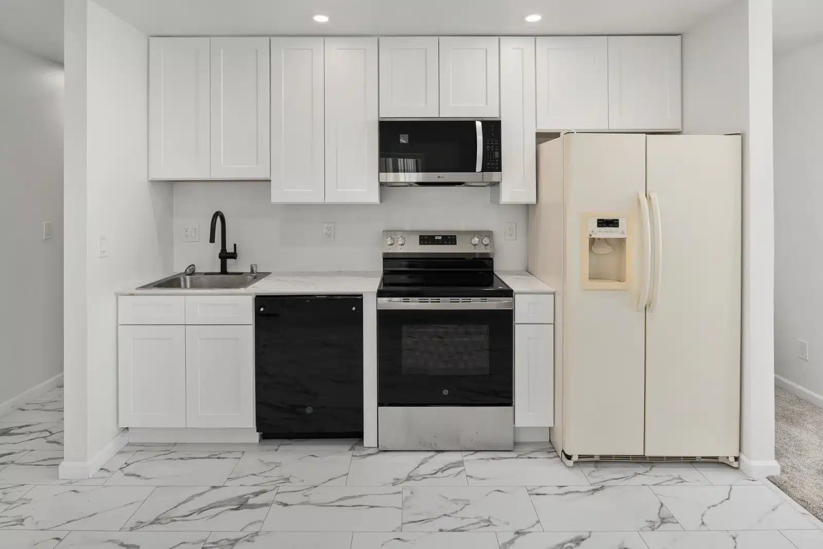 The kitchen wall with white shaker cabinets, a stainless range and microwave, and a black faucet