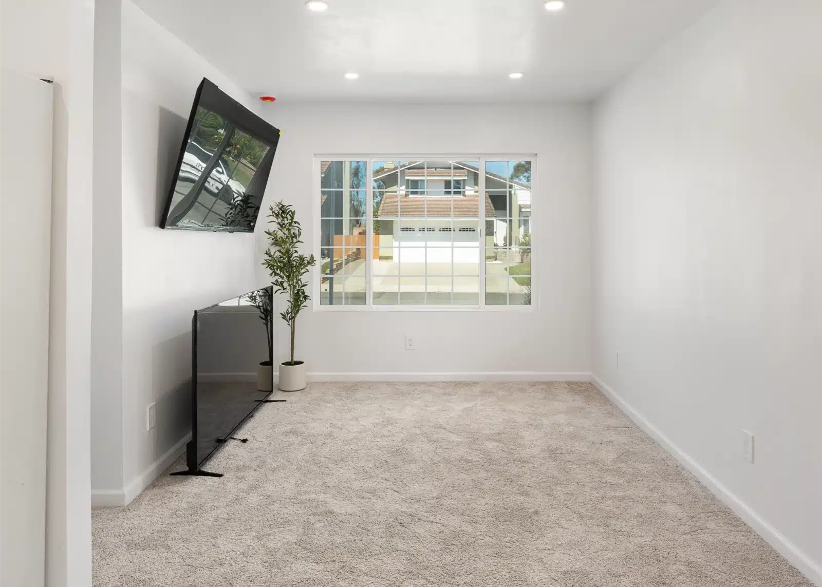 Carpeted living room in the addition with a wall-mounted television and a window to the street