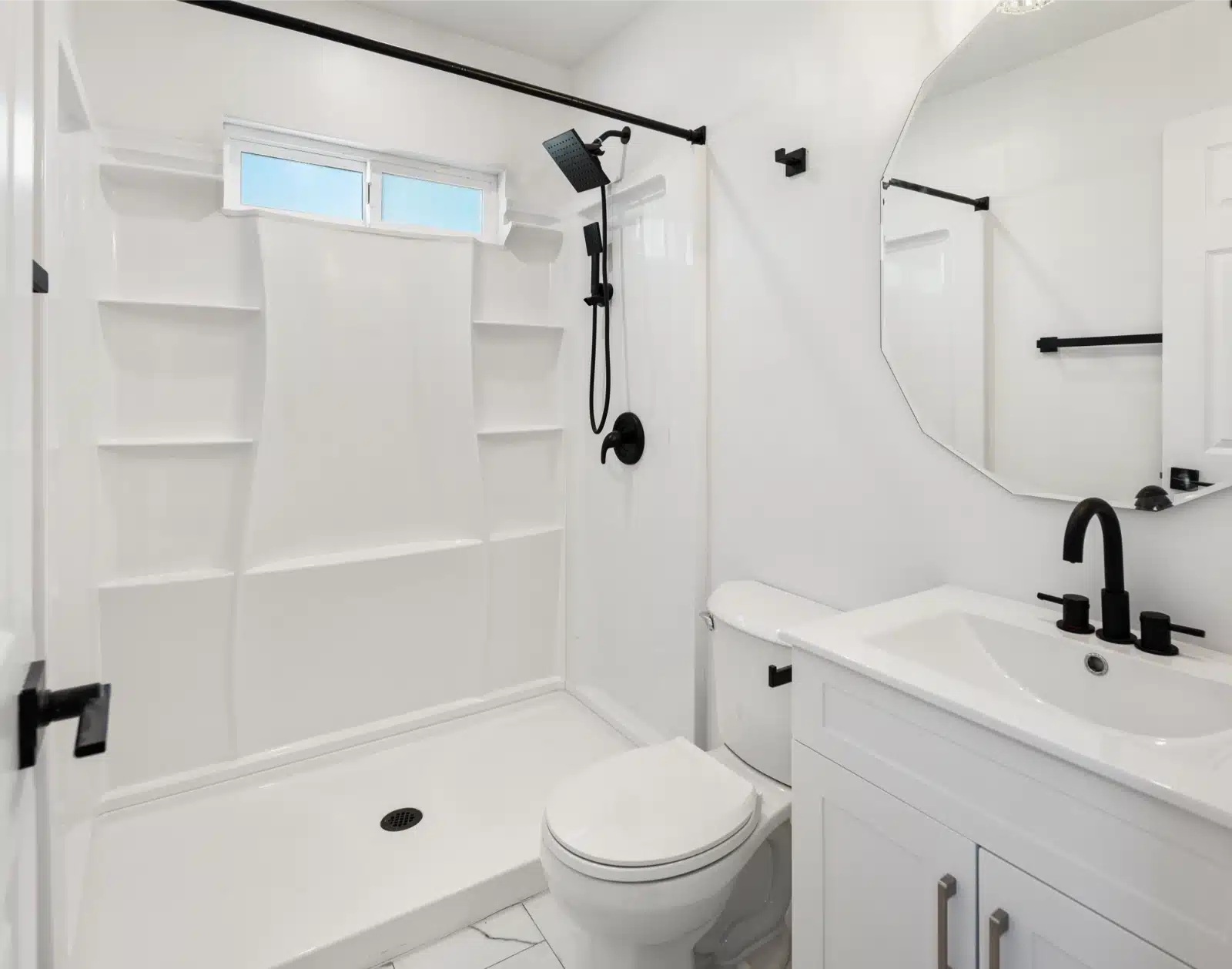 Bathroom in the addition with a shower surround, black fixtures and a round mirror