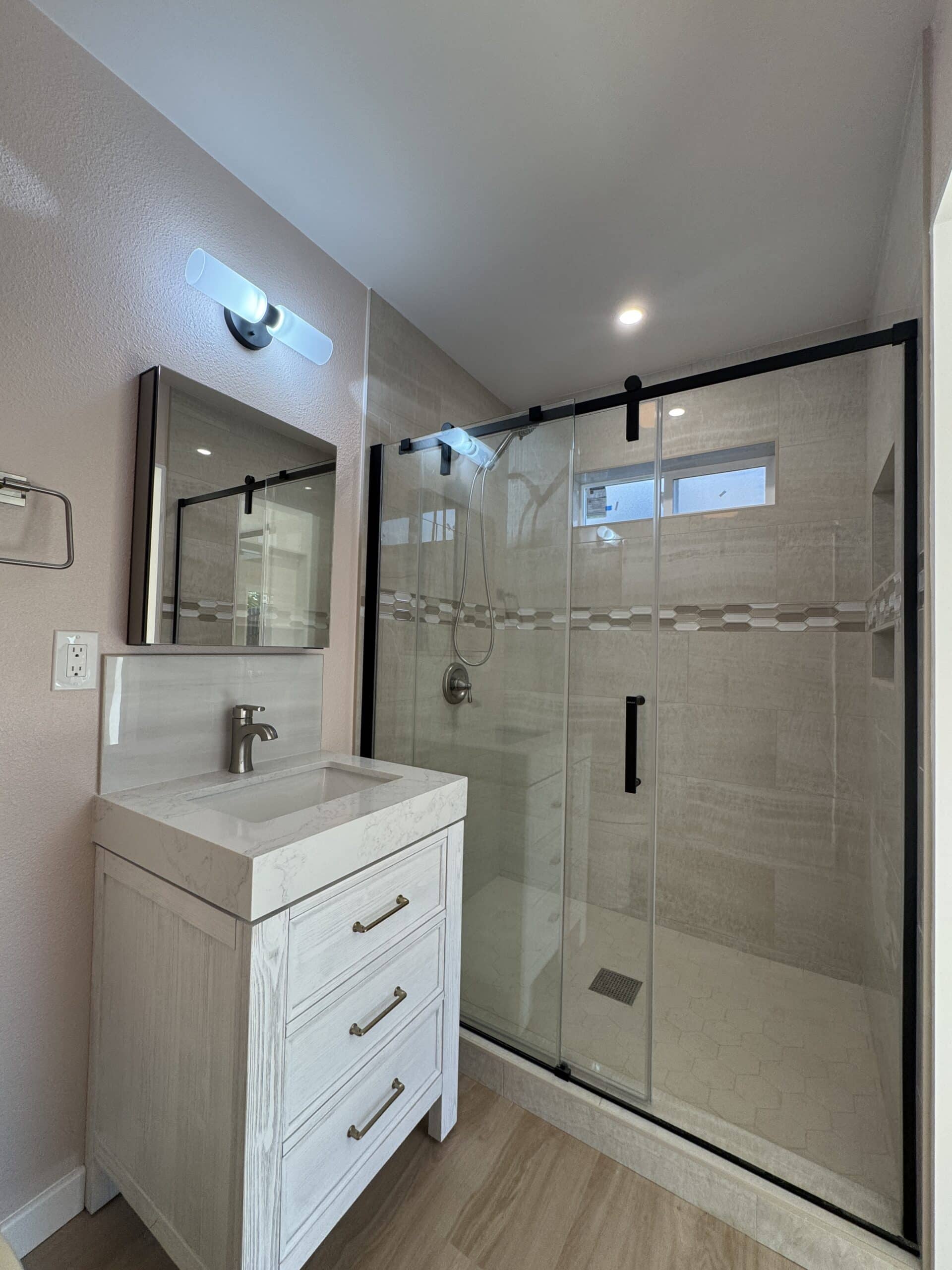 ADU bathroom with a white vanity, framed mirror and glass-enclosed shower, from a Sheiner Construction ADU in La Mesa