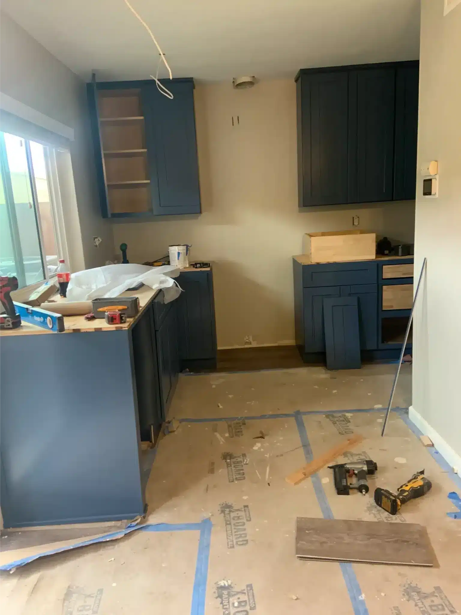Blue kitchen cabinets being installed with loose doors, staged materials, and protected flooring