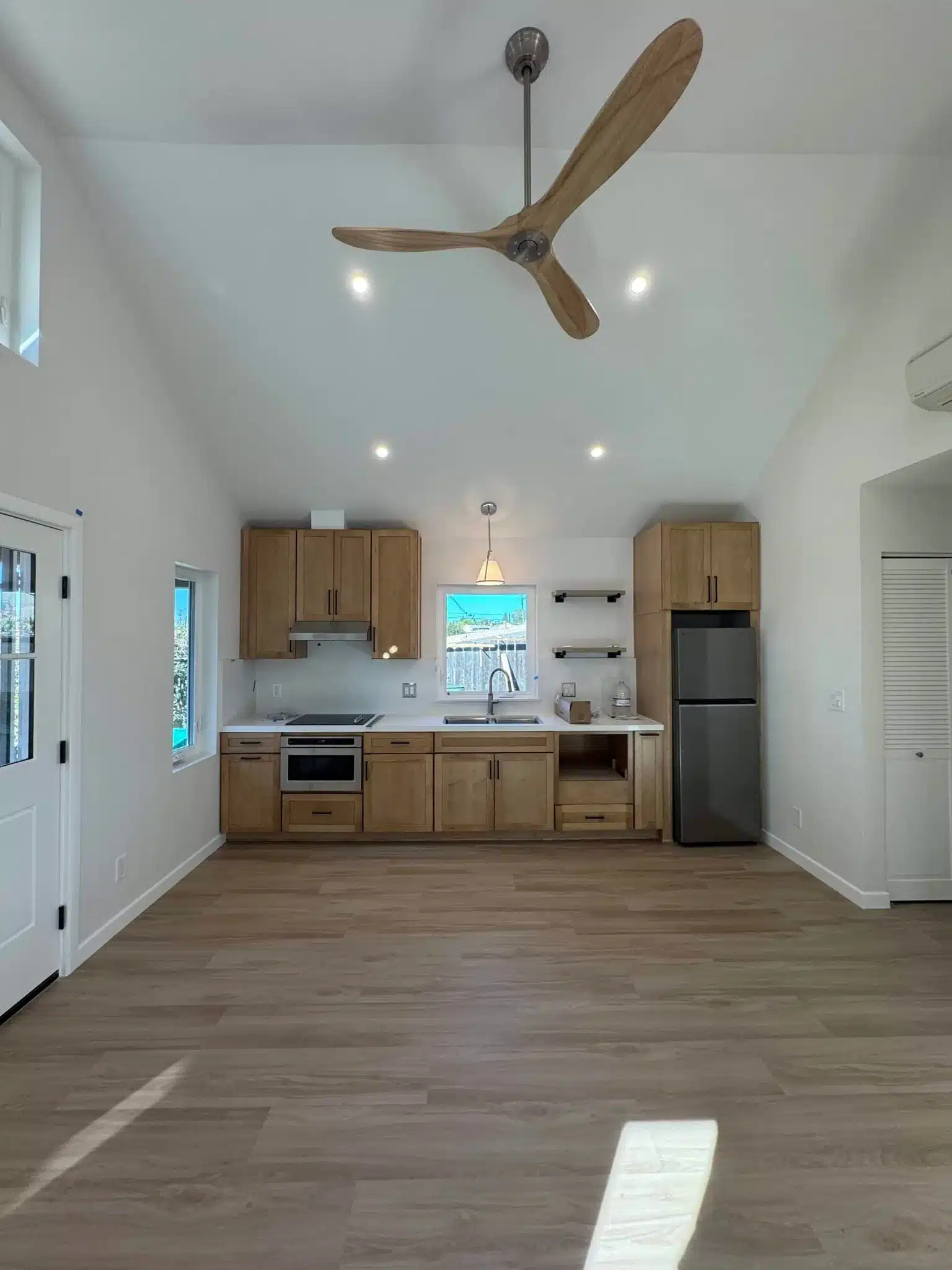 Modern kitchen with light wood cabinetry, stainless appliances, and wood-blade ceiling fan overhead.