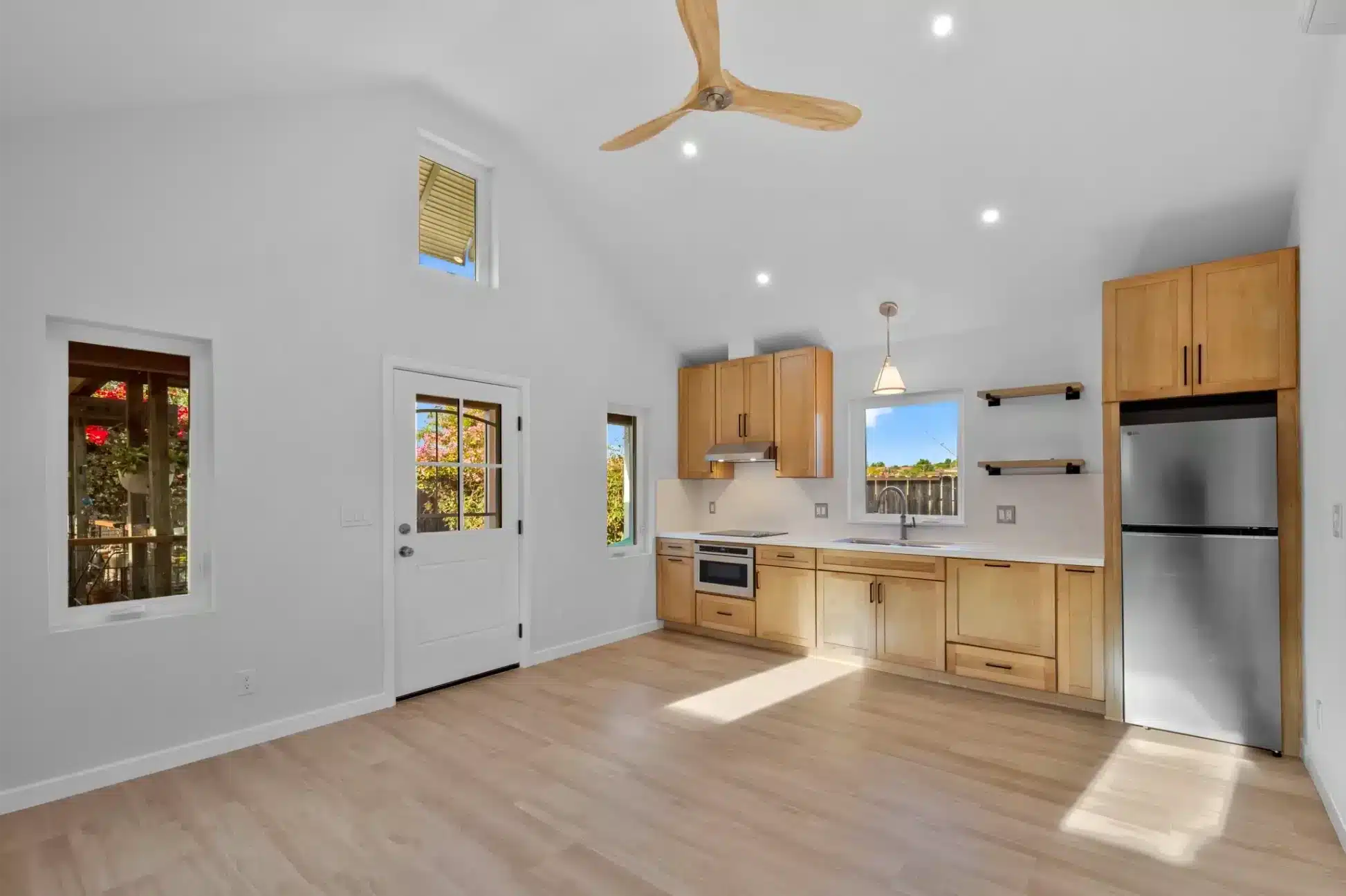 Modern kitchen with honey wood cabinetry, stainless steel appliances, white countertops, recessed lights, and wood plank